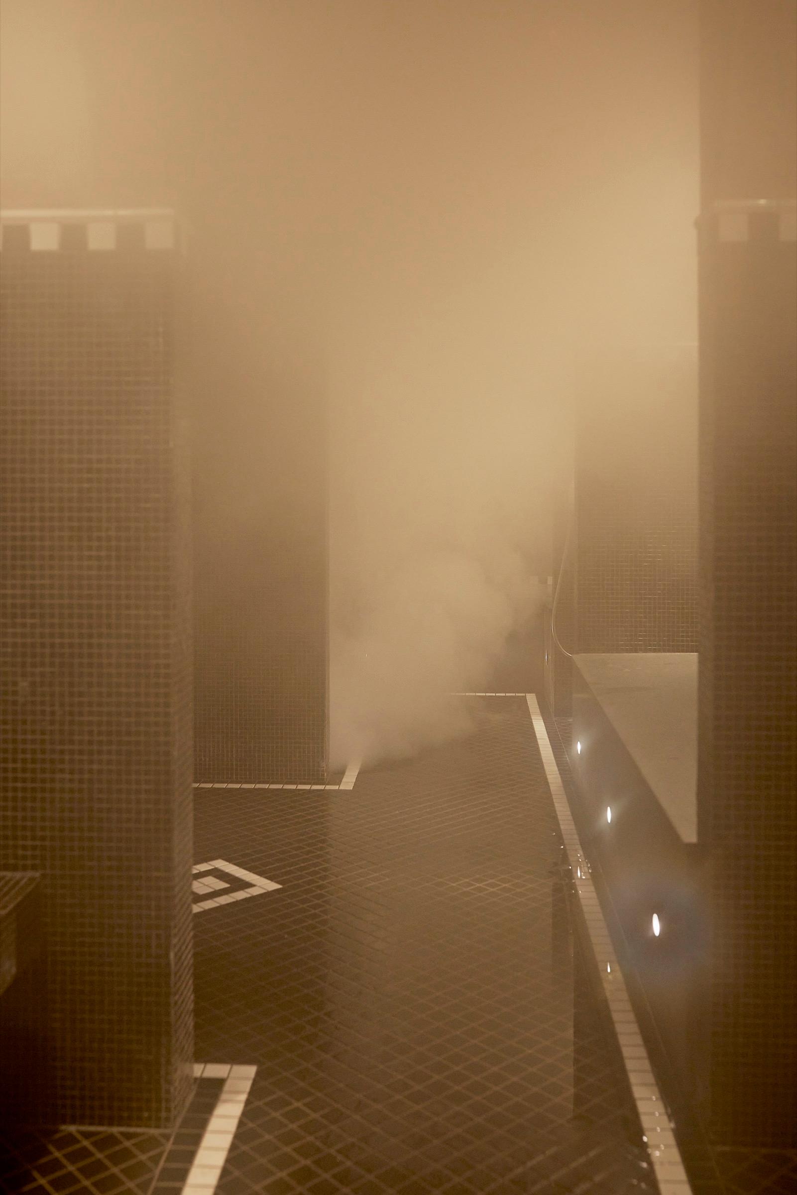 Steam fills a tiled room with square pillars and a dark tiled floor marked with pale inlaid lines.