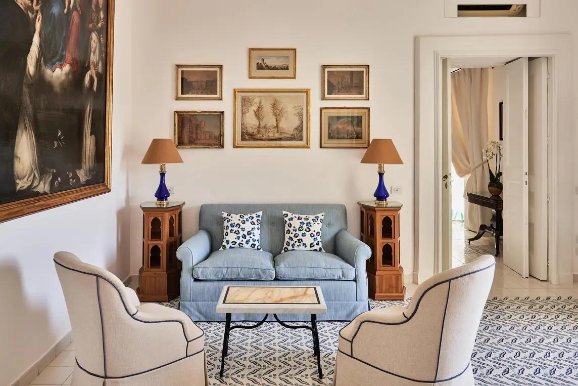 A sitting room with blue sofas, framed prints and antique chairs around a low table.