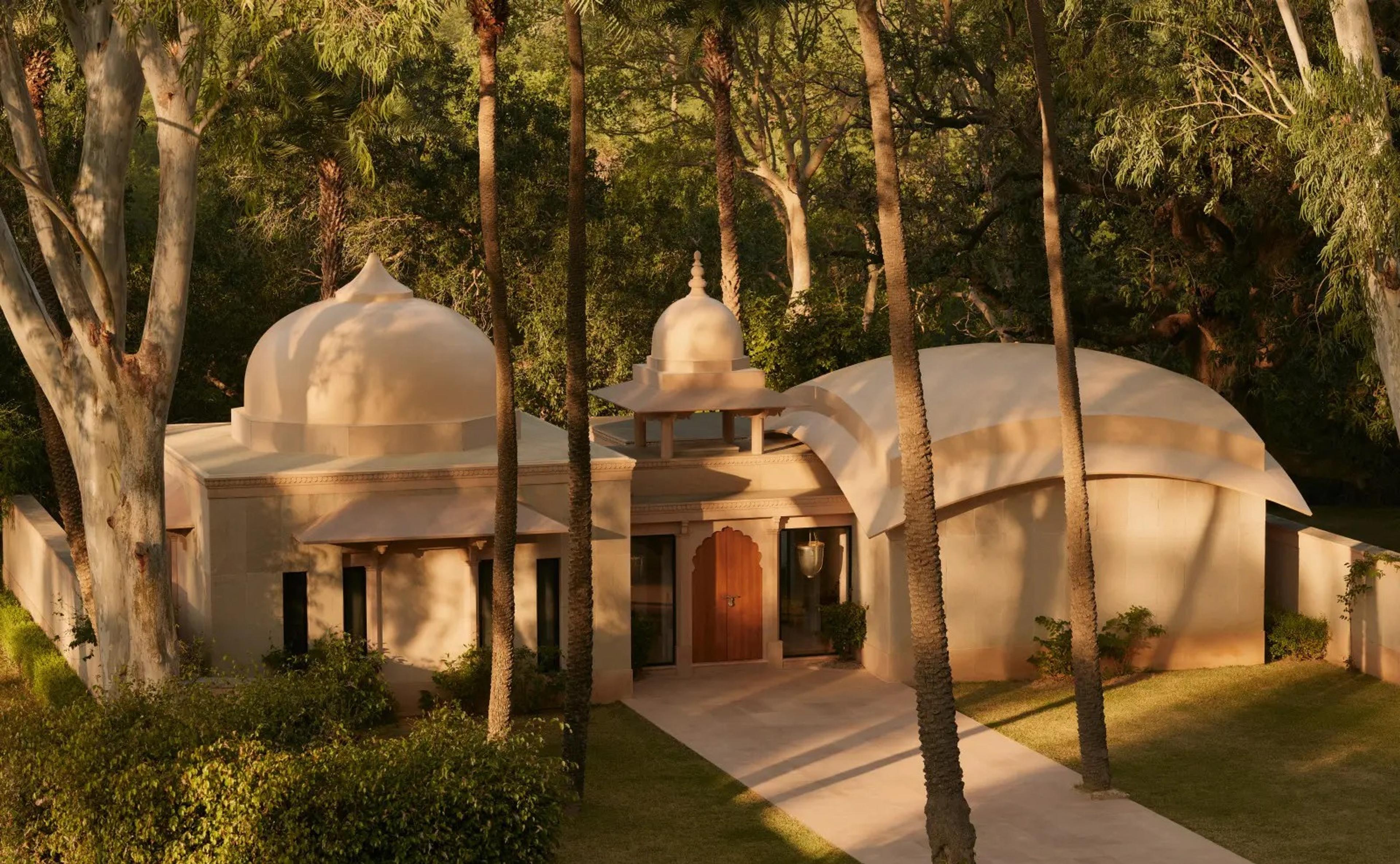 A domed stone guest pavilion set among tall trees, with a wooden door and a stone path leading to it.
