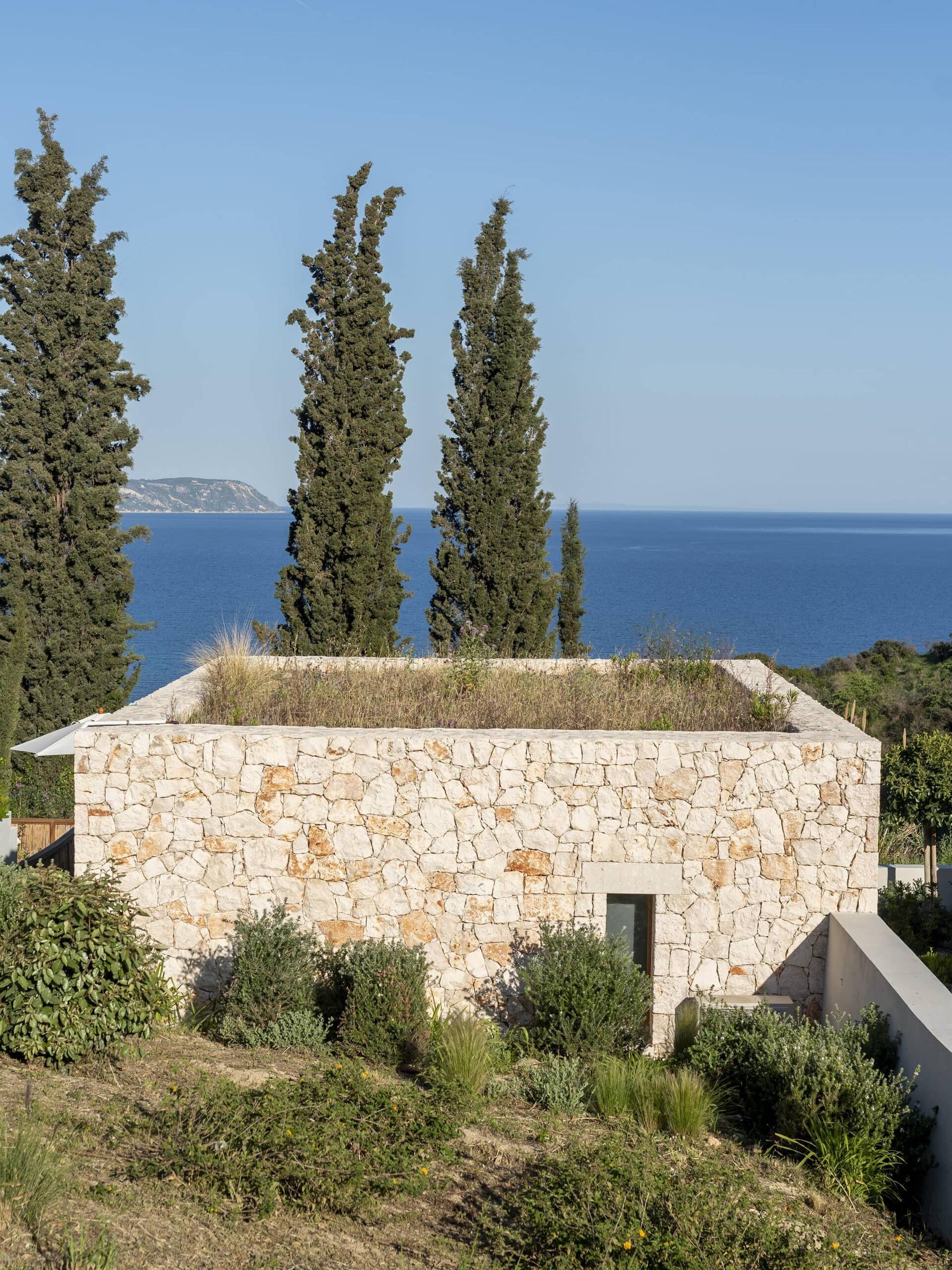 a close view of a stone building's corner with cypress trees beside it and the sea behind