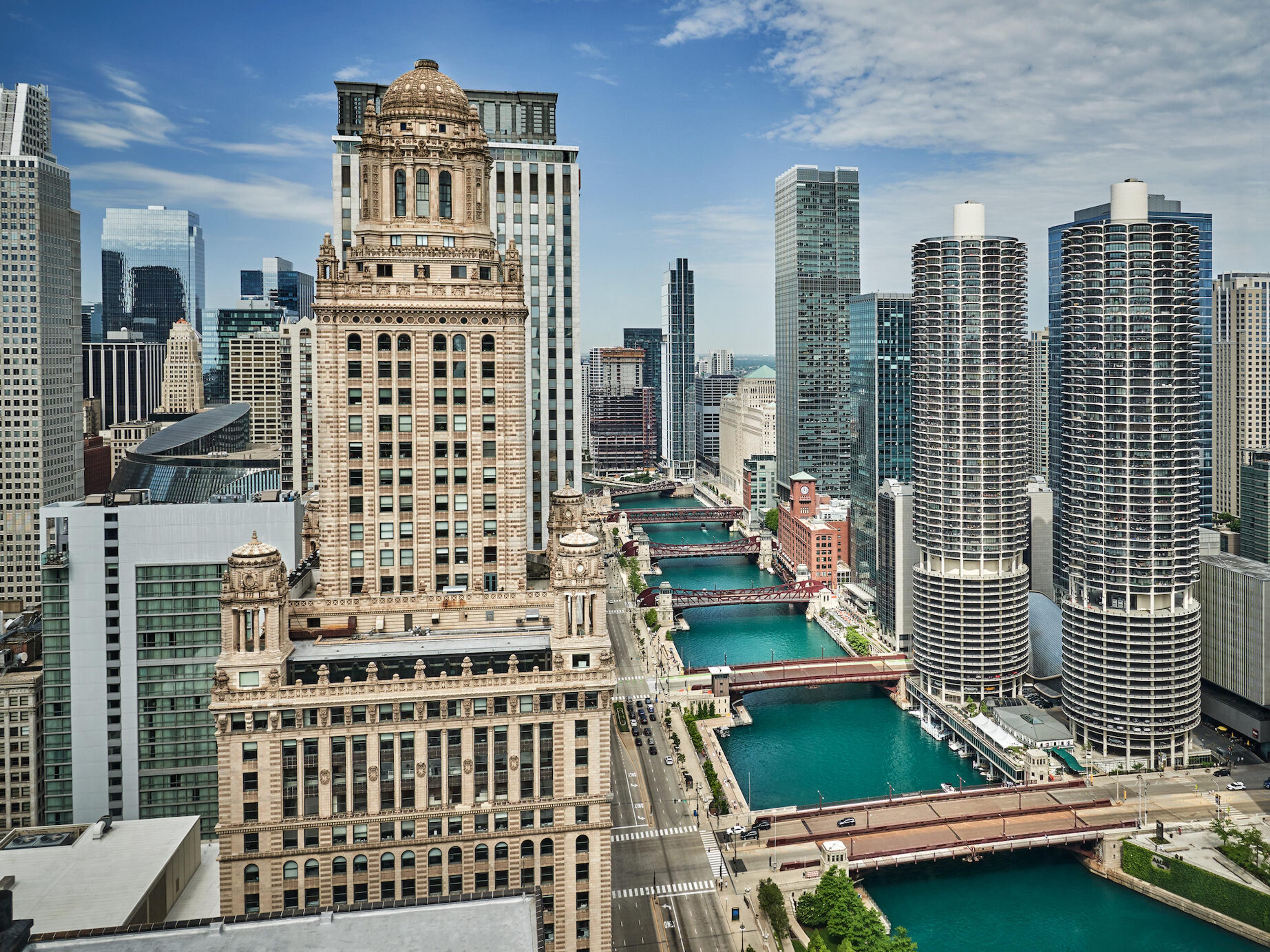An aerial view of the Chicago River lined with bridges and skyscrapers, including a domed tower and the twin cylindrical Marina City towers.