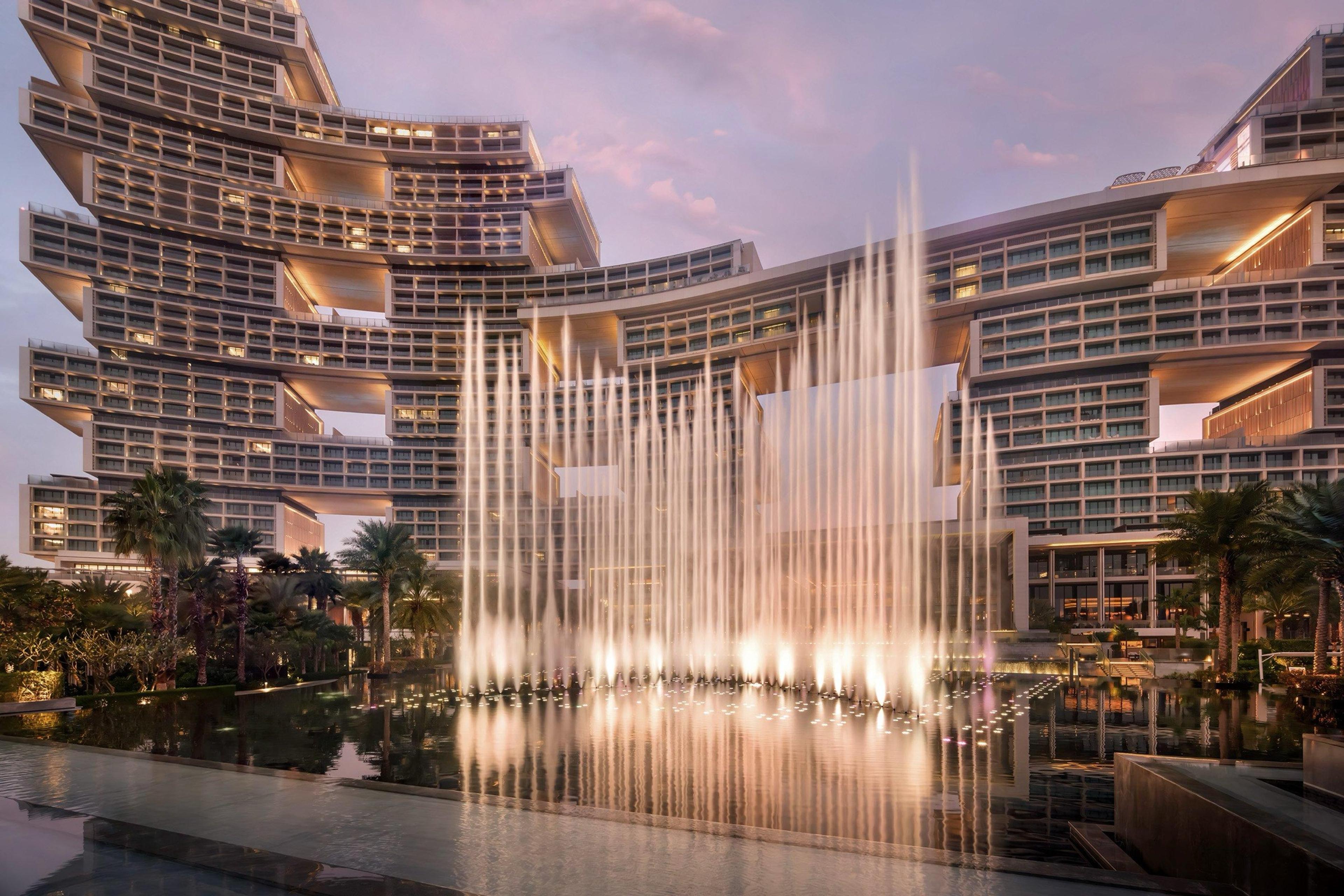 The hotel's towers at dusk behind a choreographed fountain show throwing jets of lit water into the air.