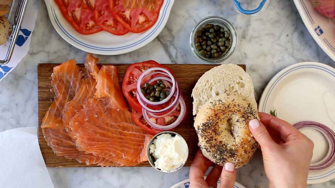 Smoked salmon, a bagel, tomato, red onion and capers on a marble counter