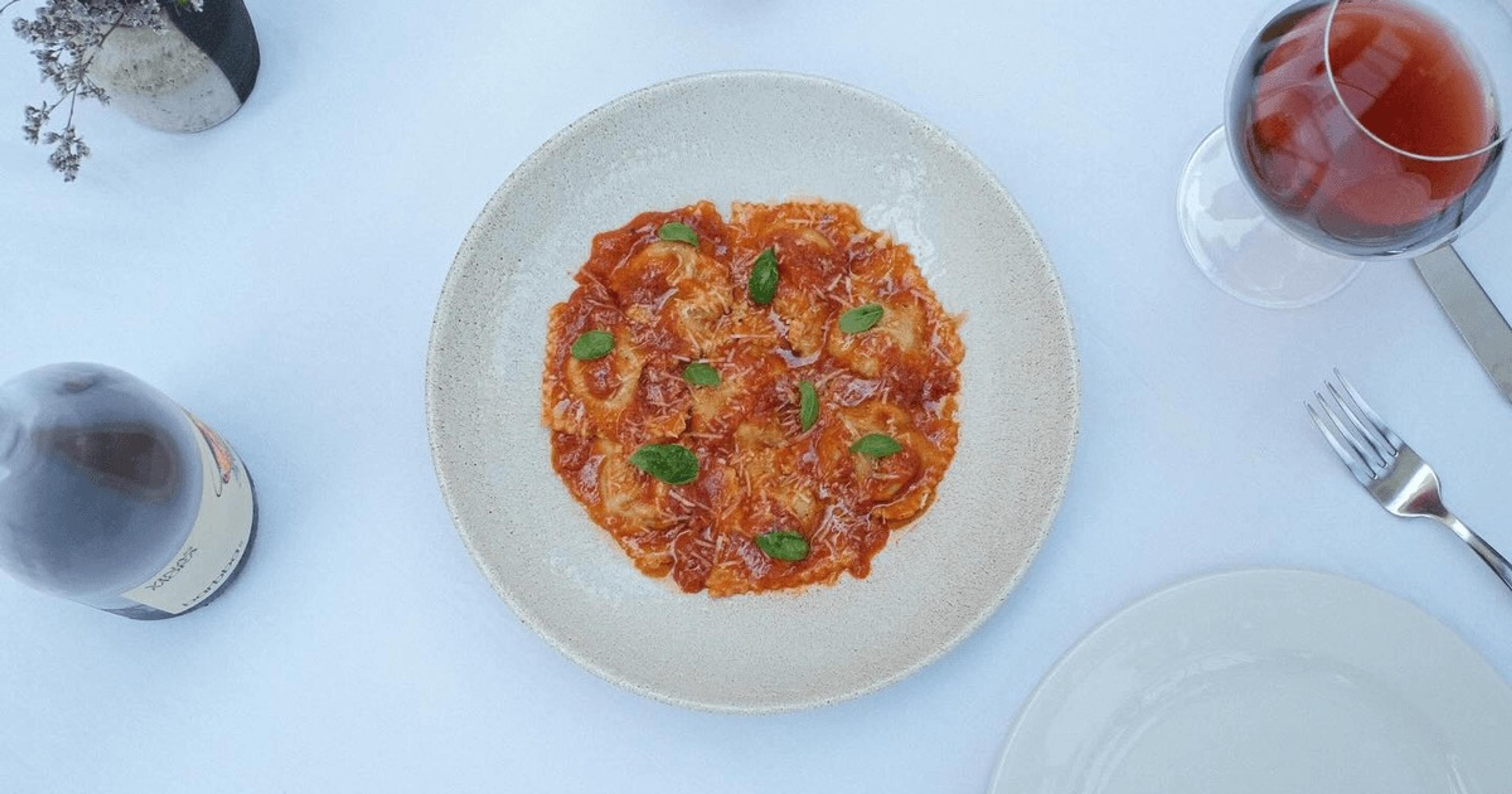 A plate of pasta in tomato sauce with basil, on a pale blue table