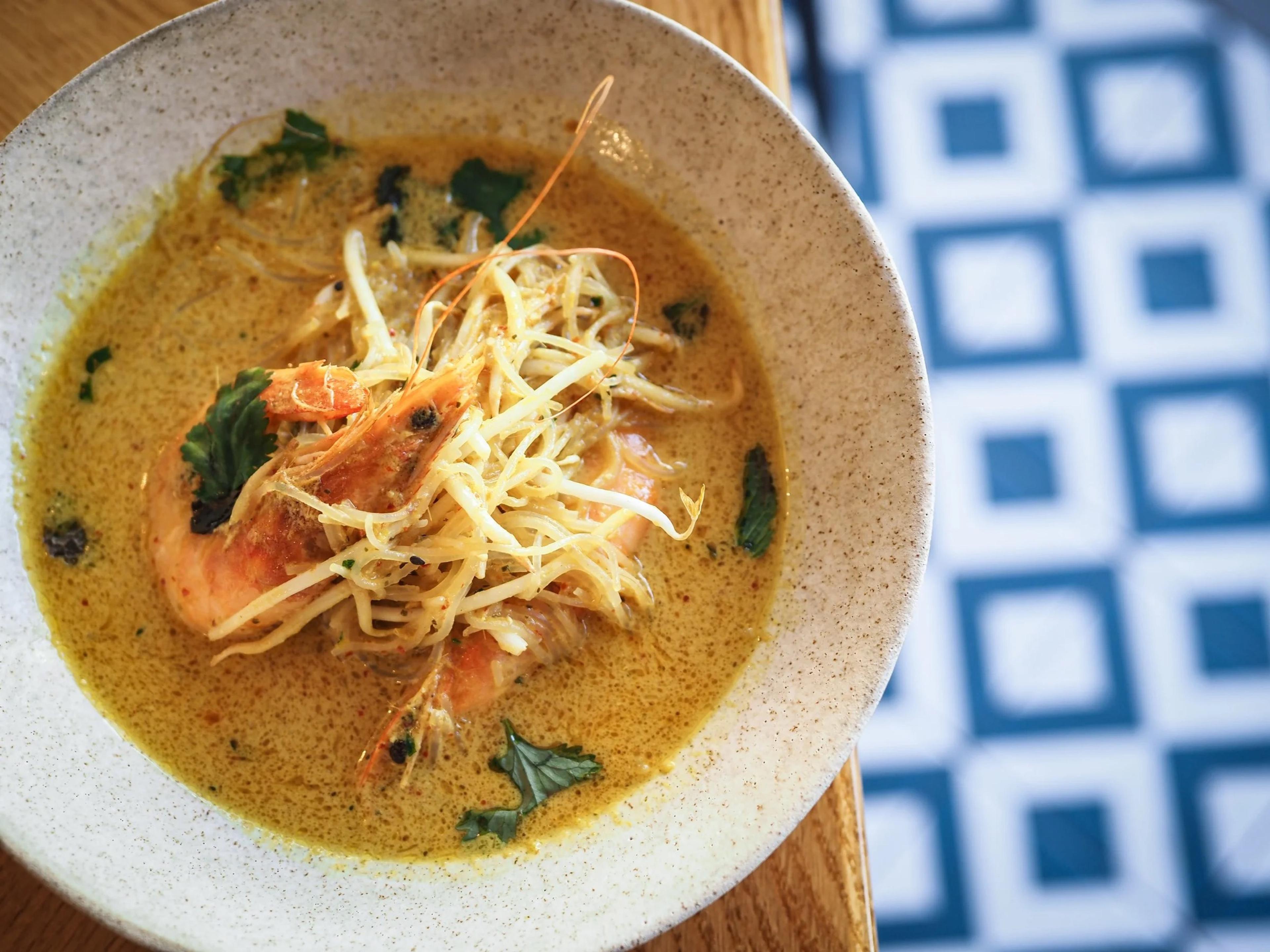 A bowl of fish in a golden broth on a blue and white tiled table