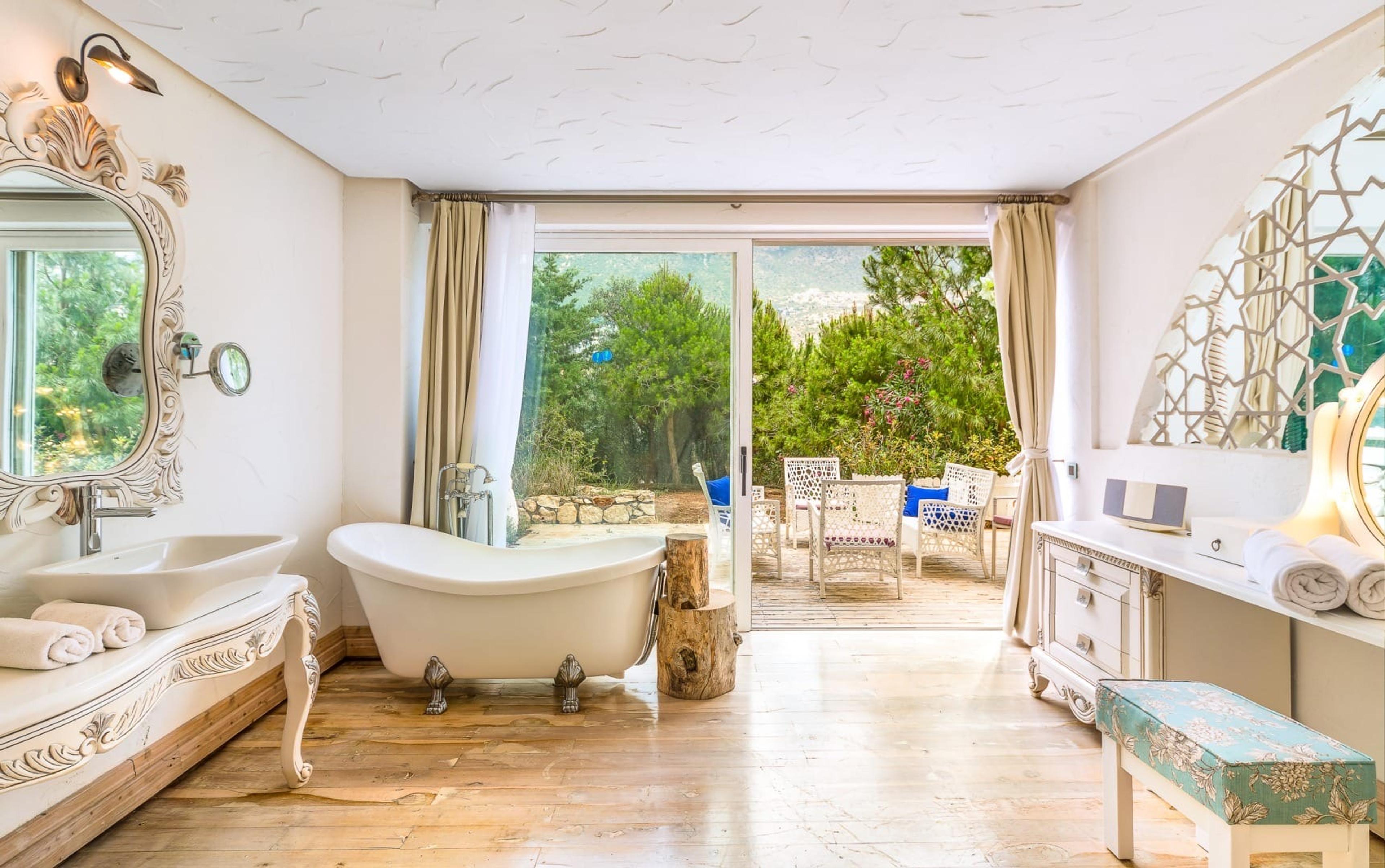 A bathroom with a freestanding clawfoot tub, a vanity, and glass doors open to a terrace with a garden and hill view.