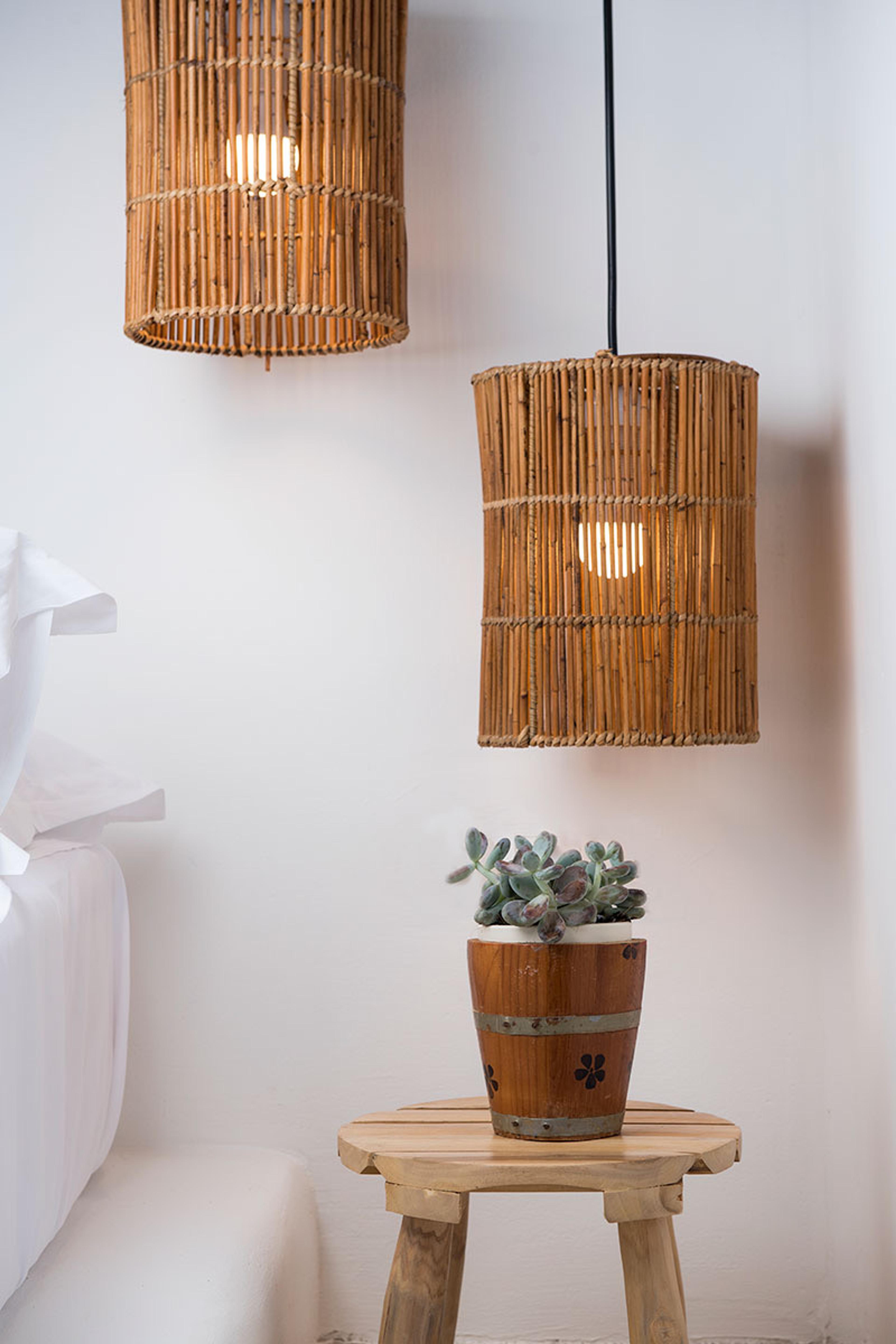 Two woven rattan pendant lamps hang over a bed with white linen, beside a round wooden stool holding a potted succulent.