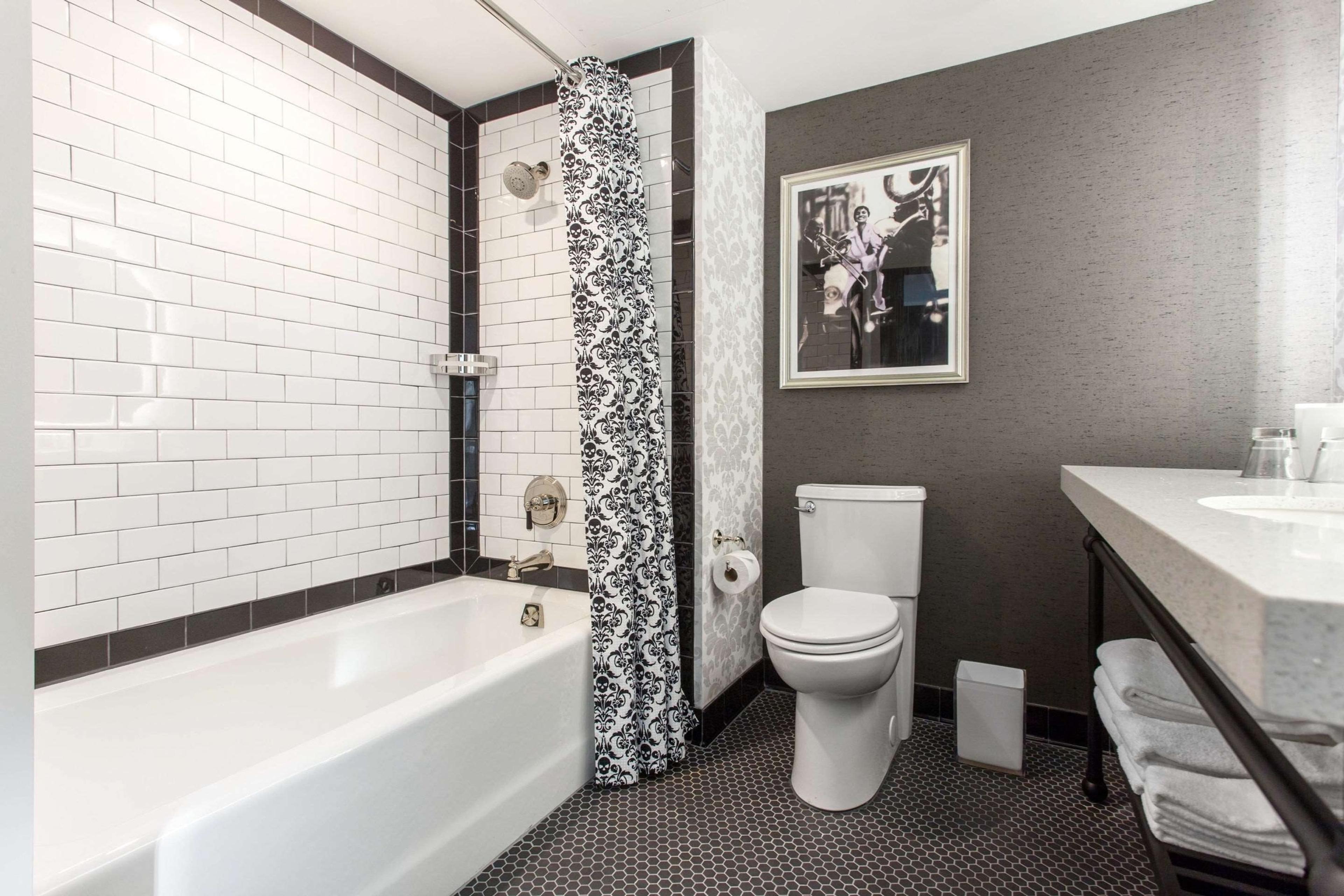 A bathroom with white subway tile around the tub, a black and white patterned shower curtain, and a framed photograph of a jazz musician on the wall.