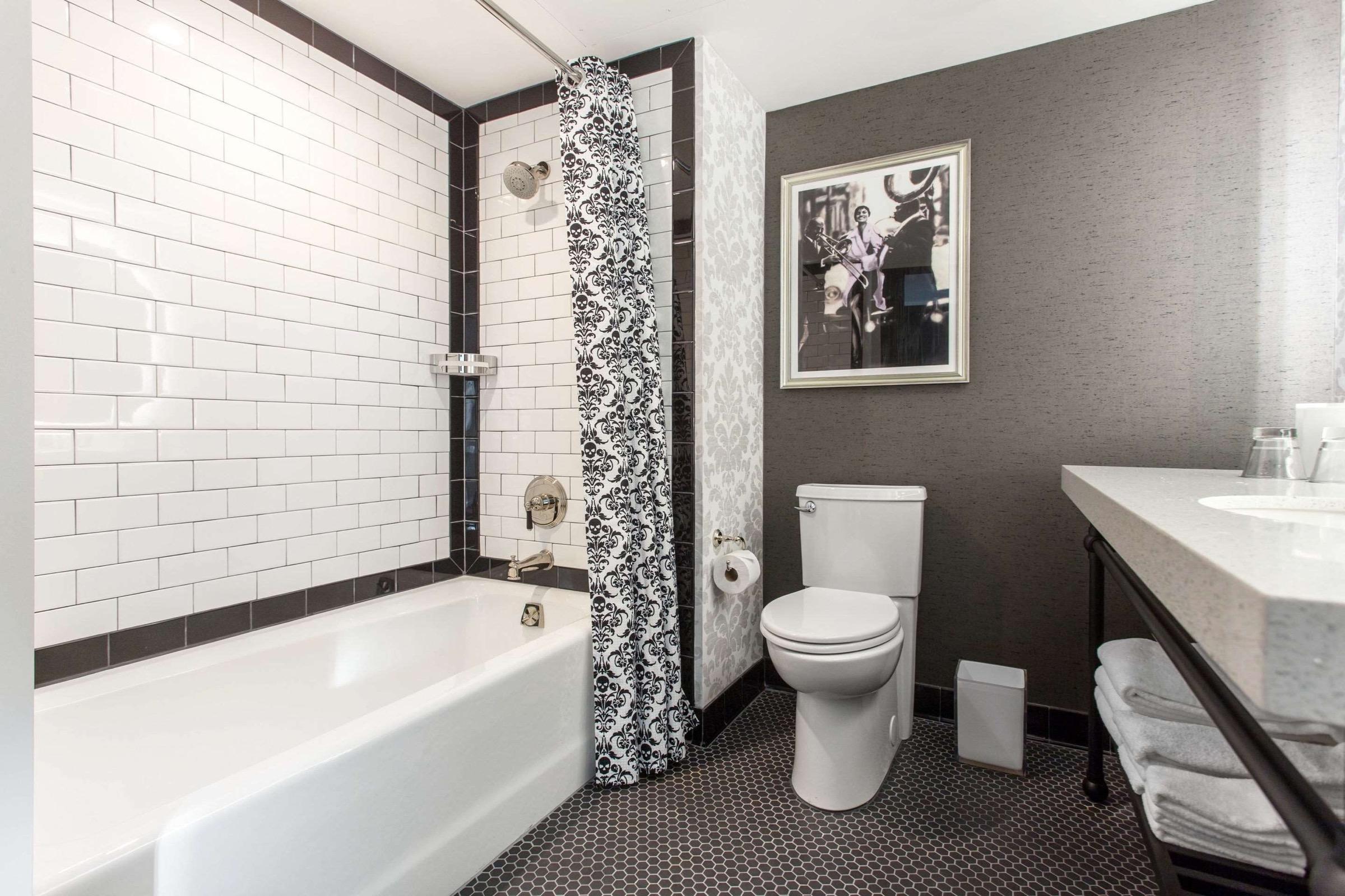 A bathroom with white subway tile around the tub, a black and white patterned shower curtain, and a framed photograph of a jazz musician on the wall.