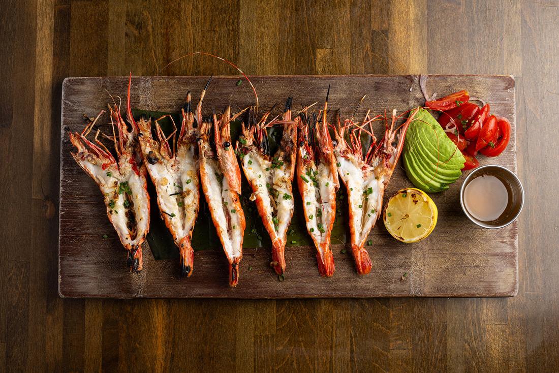 Grilled prawns split and laid out on a wooden board with lime and avocado at Holbox