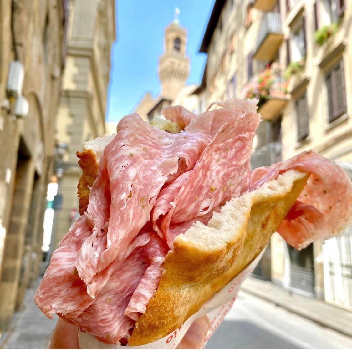A schiacciata from All'Antico Vinaio, stacked with cured meats, held up in the street