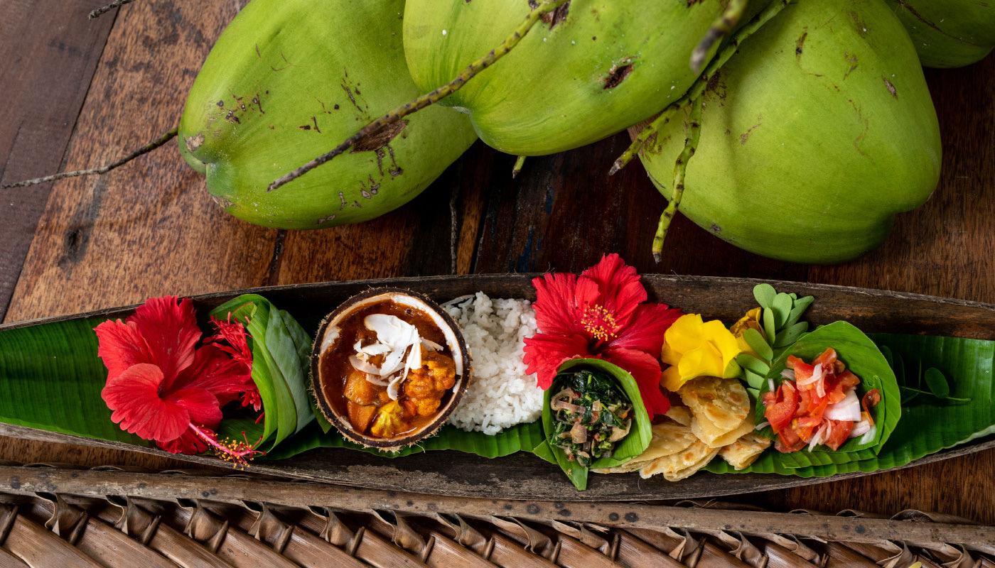 Zanzibari dishes of curry, rice and coconut chutney served in a hollowed banana leaf beside fresh green coconuts.