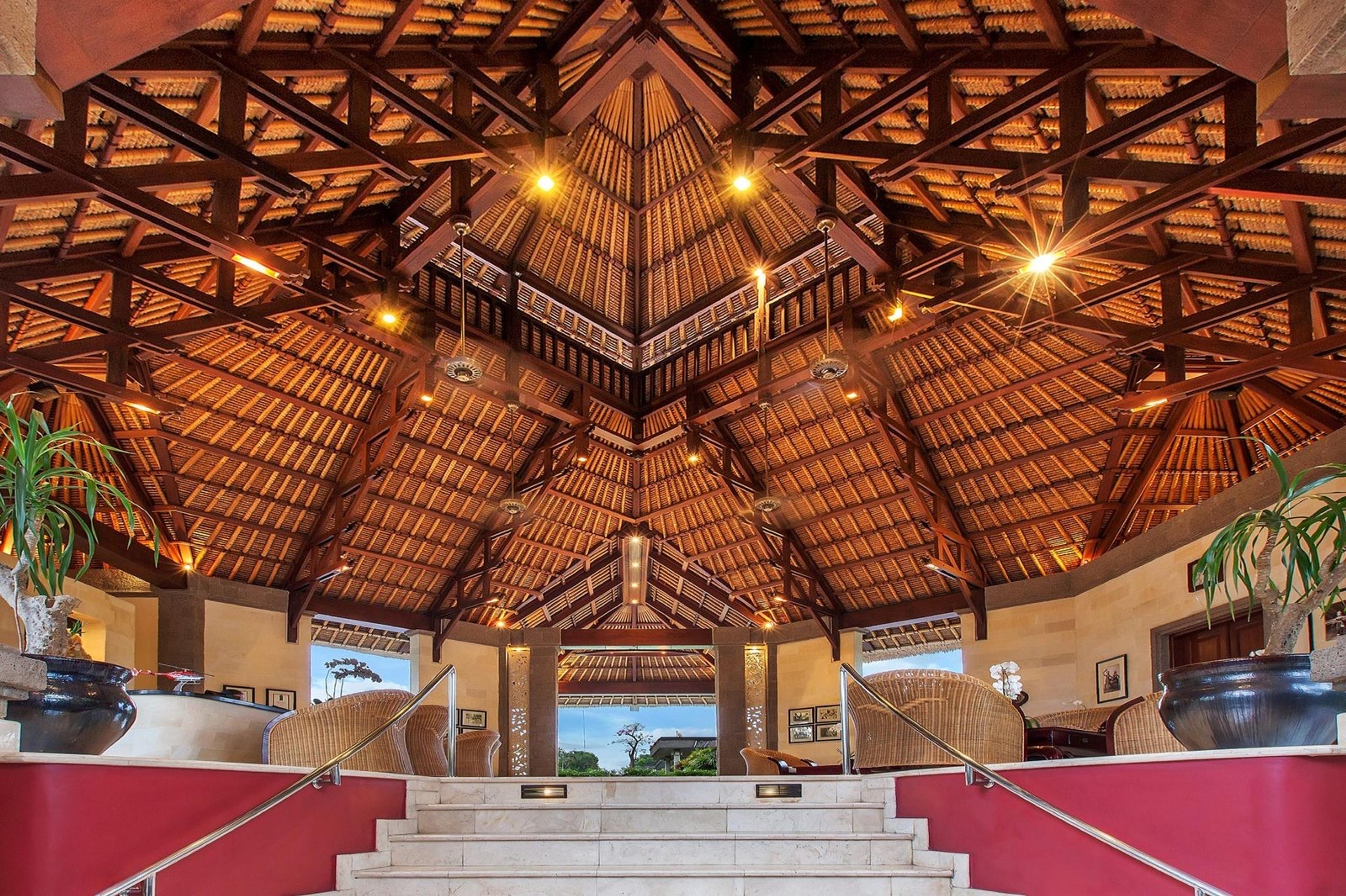 A high timber and thatch ceiling rises over a staircase into a lobby furnished with rattan chairs.