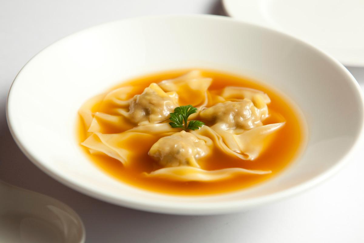 Dumplings in a clear golden broth in a white bowl