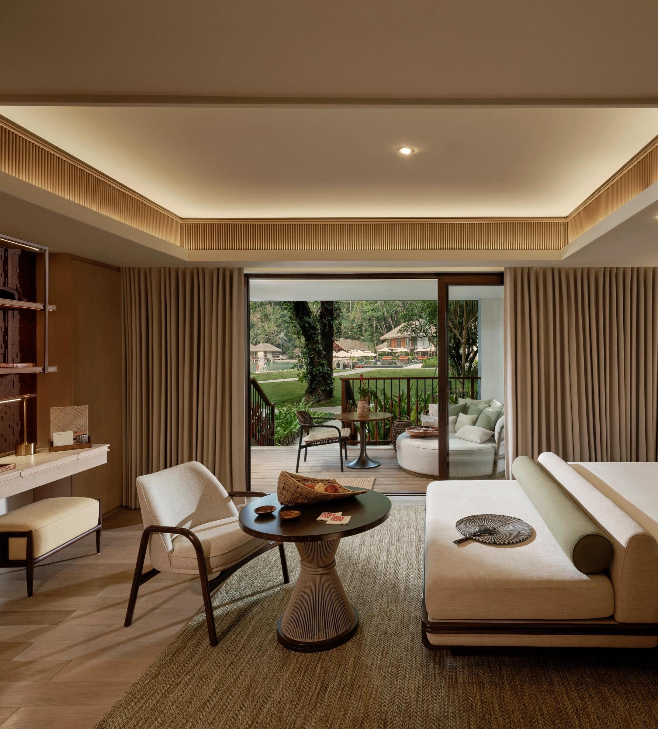 A bedroom with a low sofa and a desk, its glass doors opening onto a balcony among the trees.