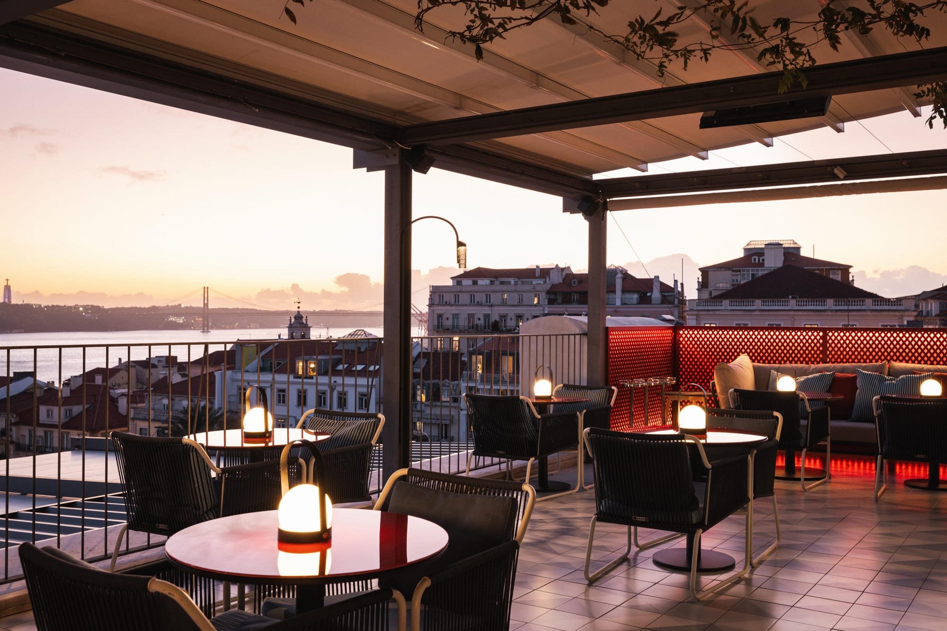 A rooftop terrace at dusk with candlelit tables and the city below