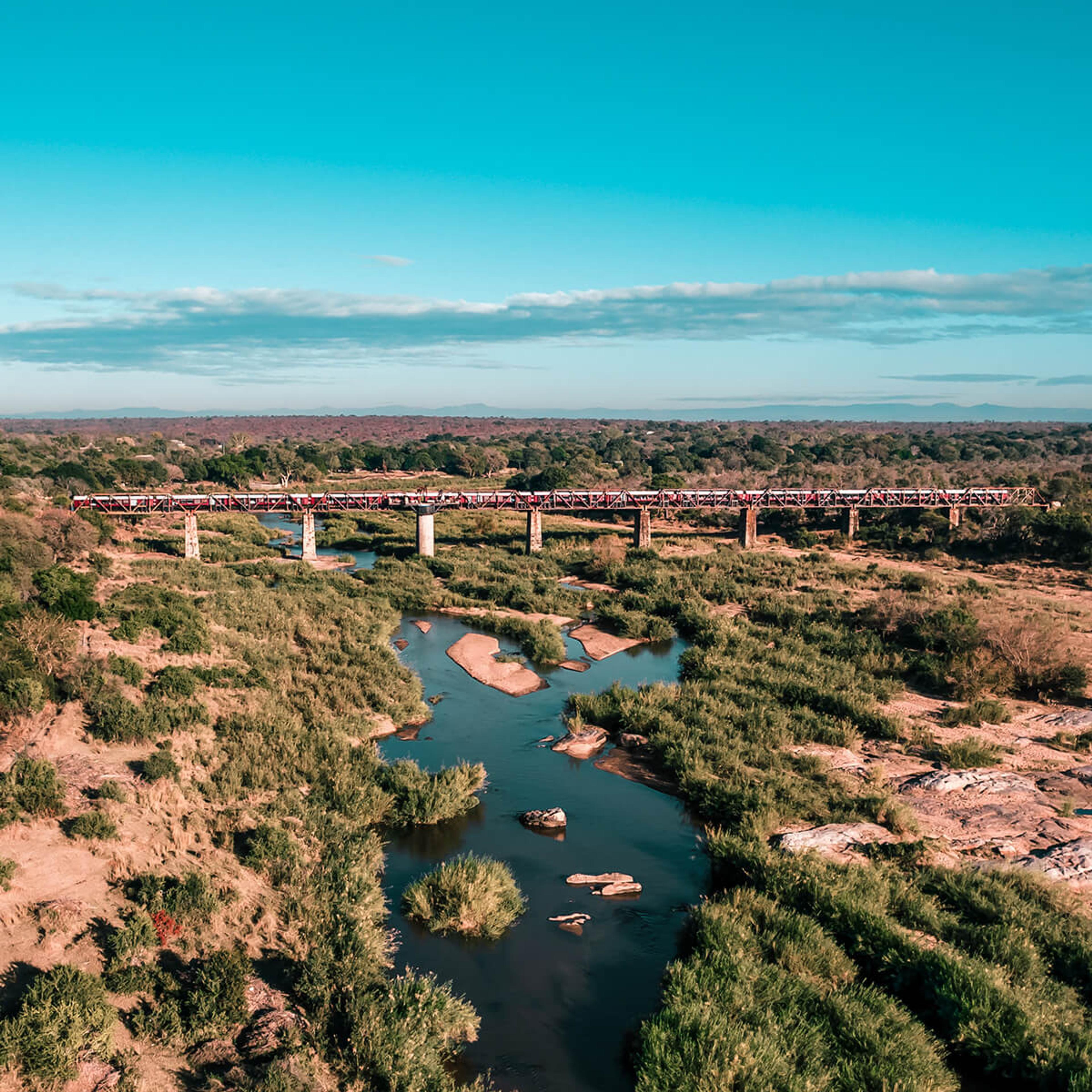 A wide aerial view of the whole steel bridge crossing the river valley, the train a thin red line against the bush.