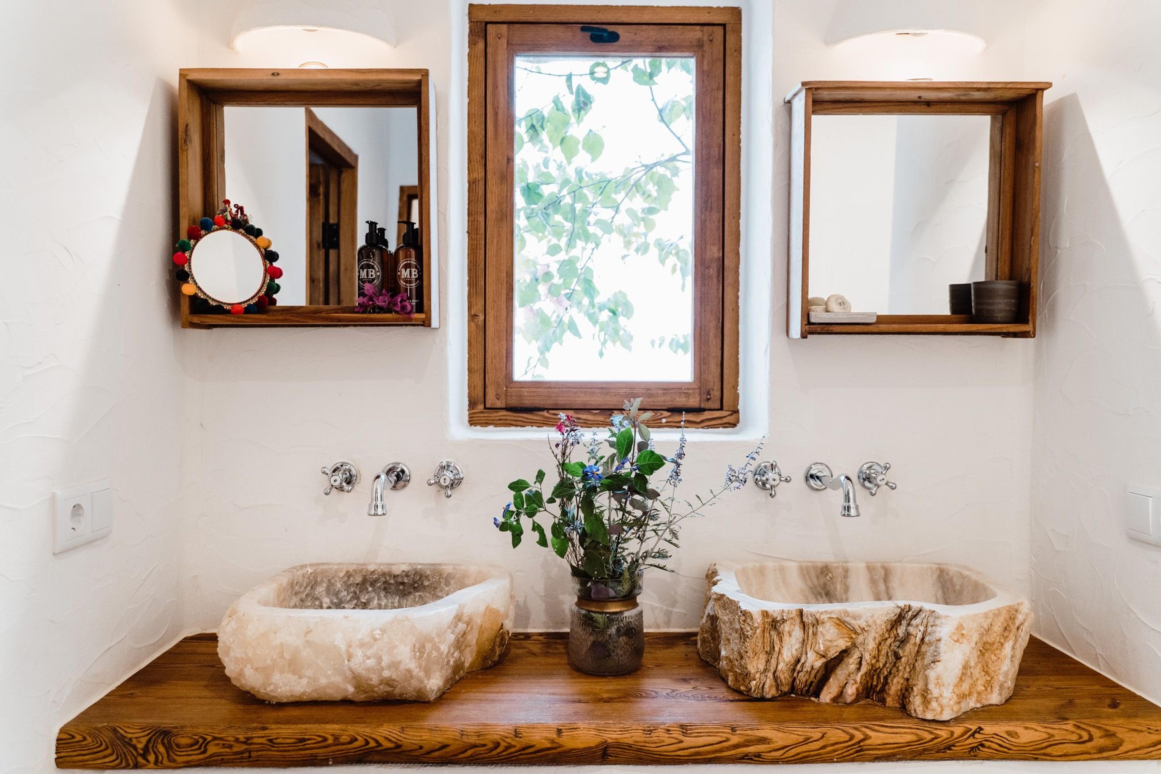 A bathroom with two stone basins set into a wooden counter, wall-mounted taps, mirrored cabinets and a small vase of wildflowers between them.