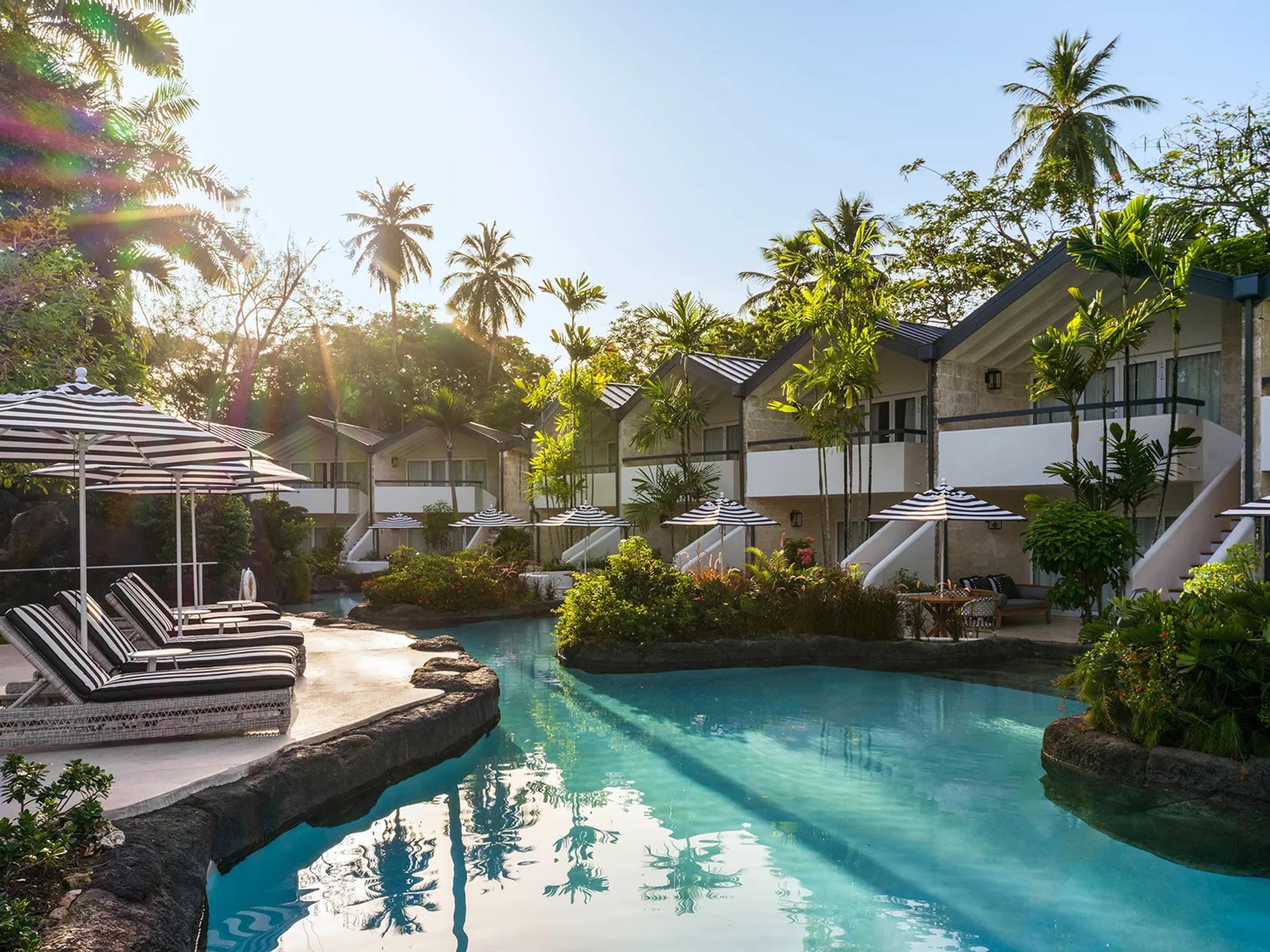A blue lagoon pool among palms and the white rooms in the morning sun