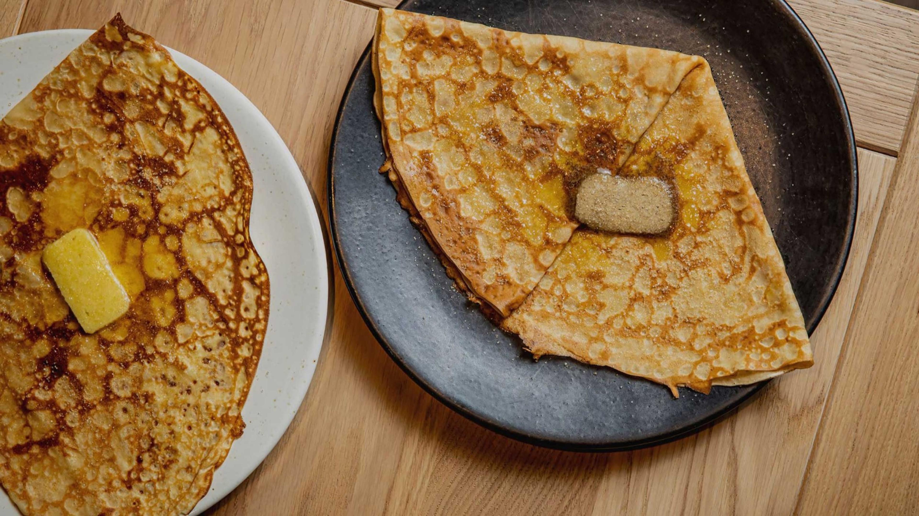 A folded buckwheat galette on a dark plate, on a wooden table.