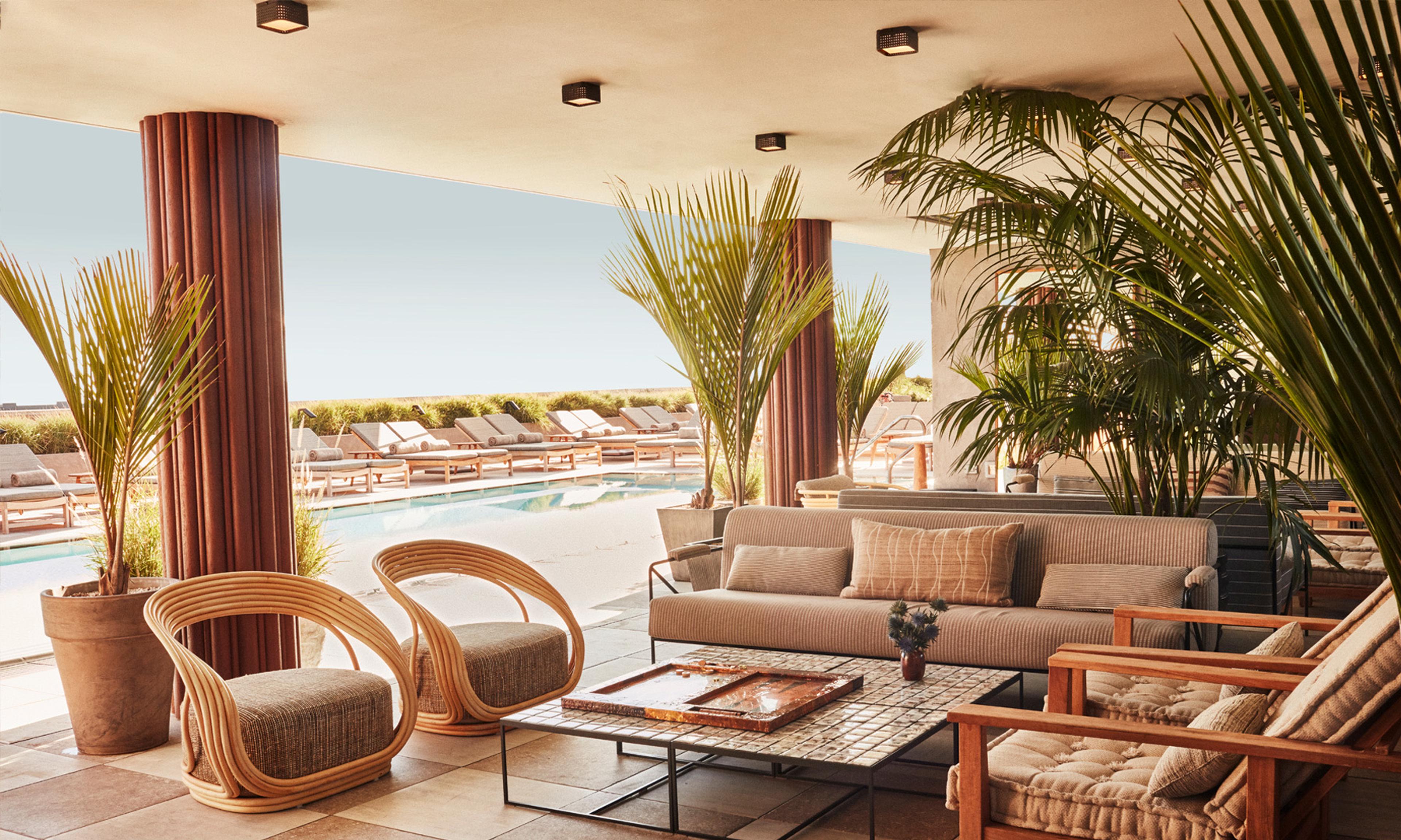 A covered terrace with rattan armchairs and a striped sofa around a tiled coffee table, looking out over a row of poolside loungers.