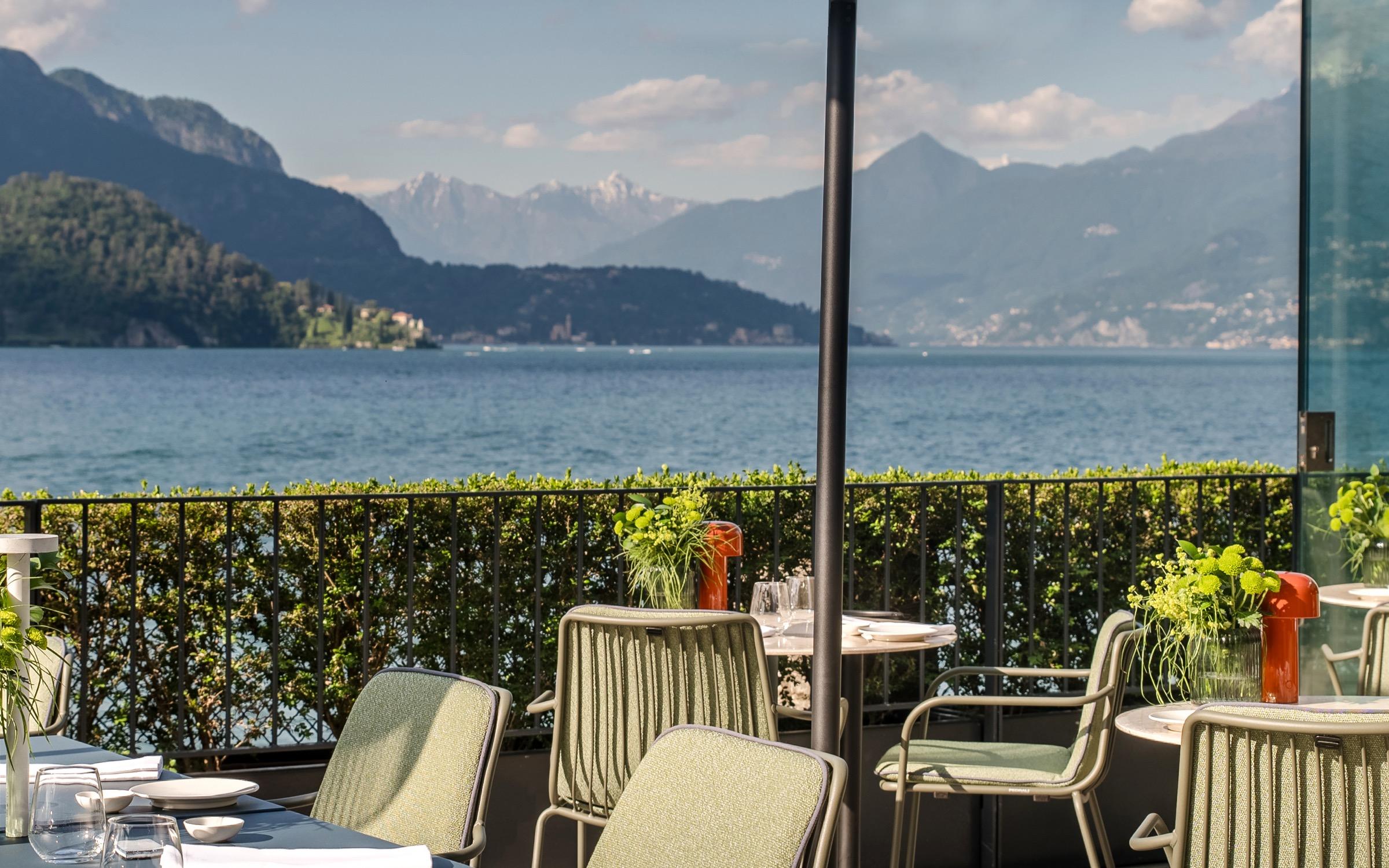 Tables and chairs on a hedged terrace above Lake Como, mountains across the water
