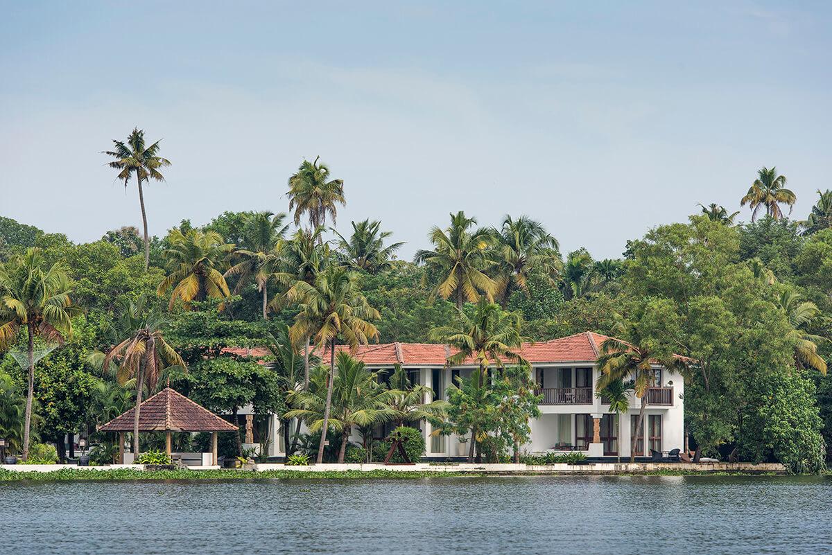 The hotel's red roofed building seen across still water, surrounded by palm trees.