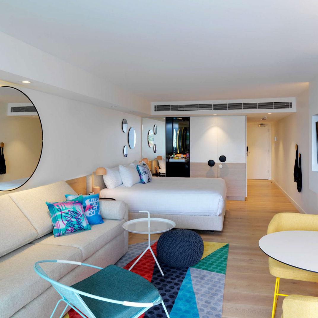 A bright room with blue cushions on white sofas and a round mirror