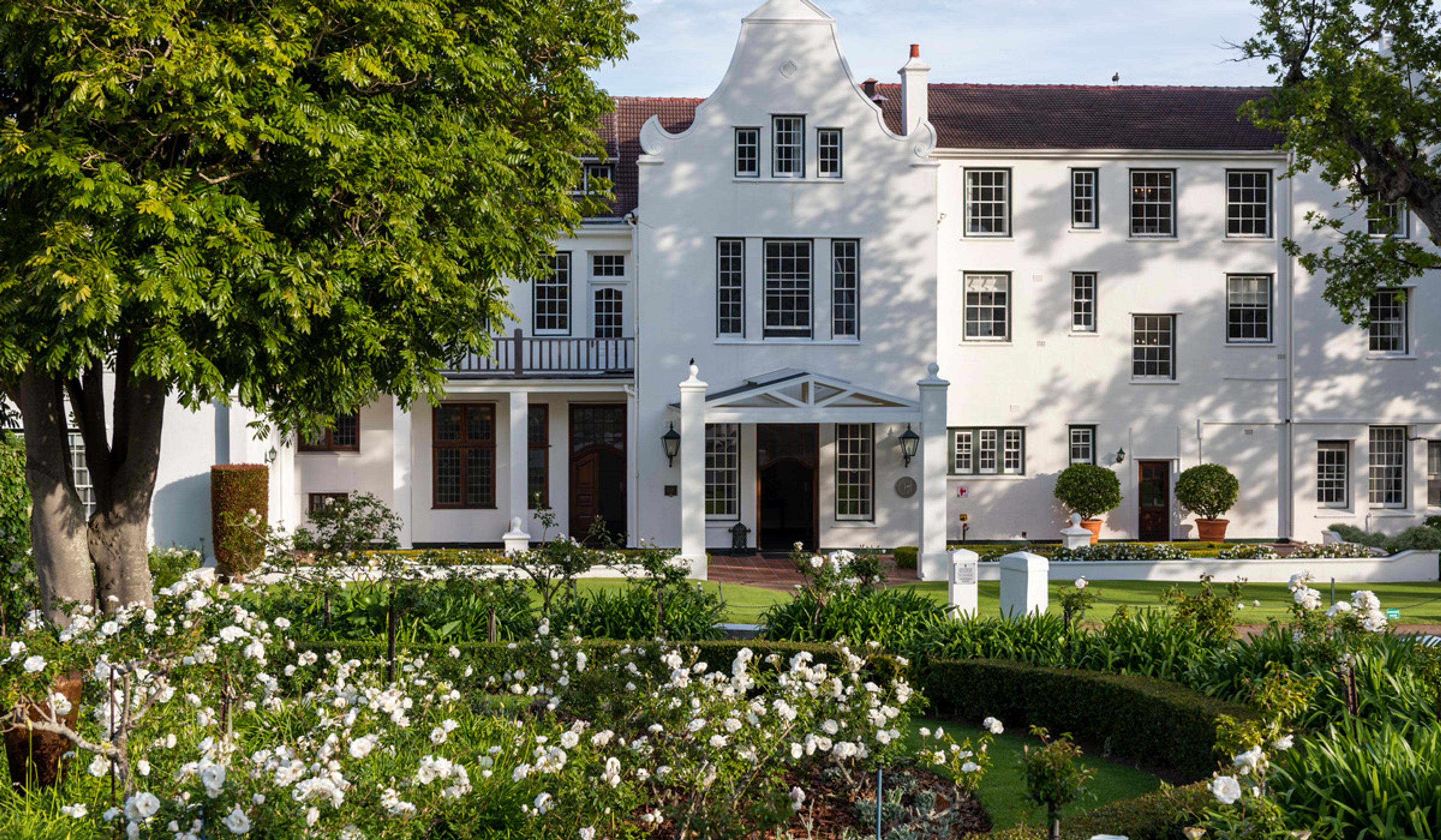 A white building with curved gables seen across a front garden of white roses, with a columned porch at the centre.