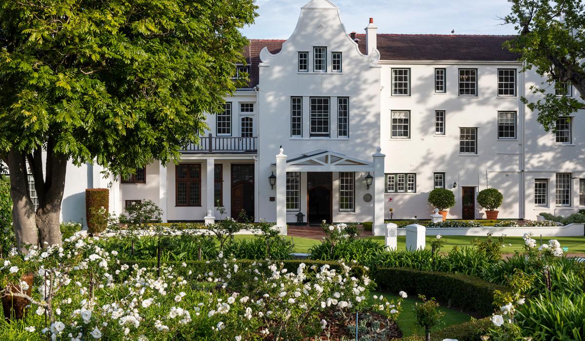 A white building with curved gables seen across a front garden of white roses, with a columned porch at the centre.