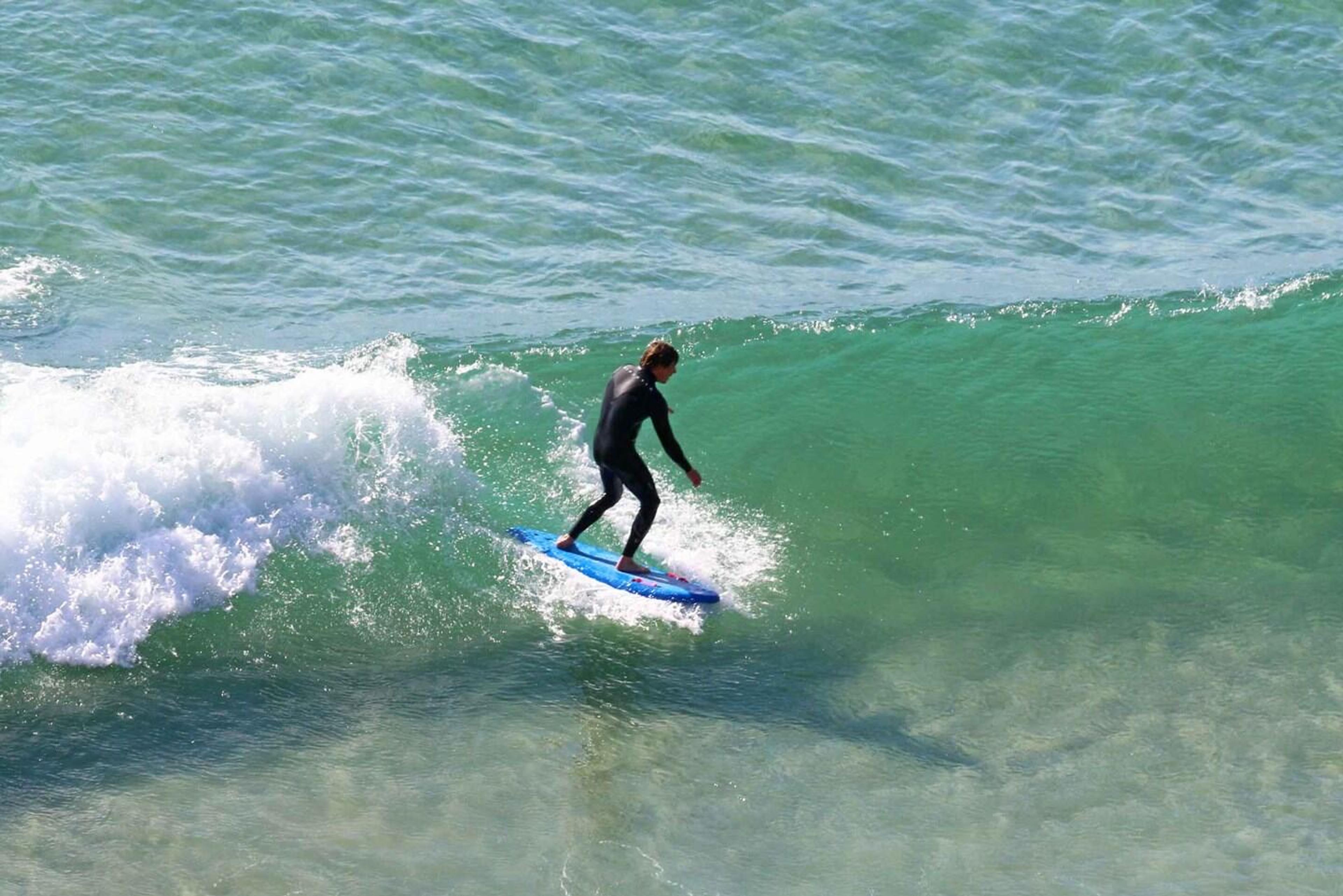 A surfer in a wetsuit riding a breaking wave, seen from above.