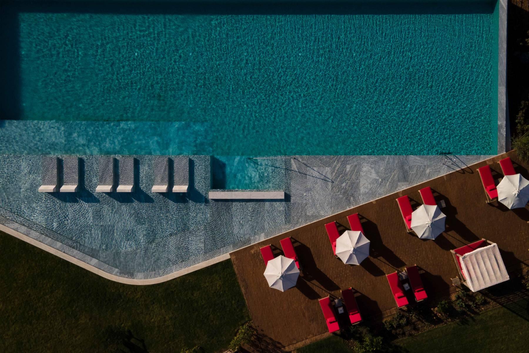 An aerial view of a rectangular pool with red sunloungers and white umbrellas along two sides.