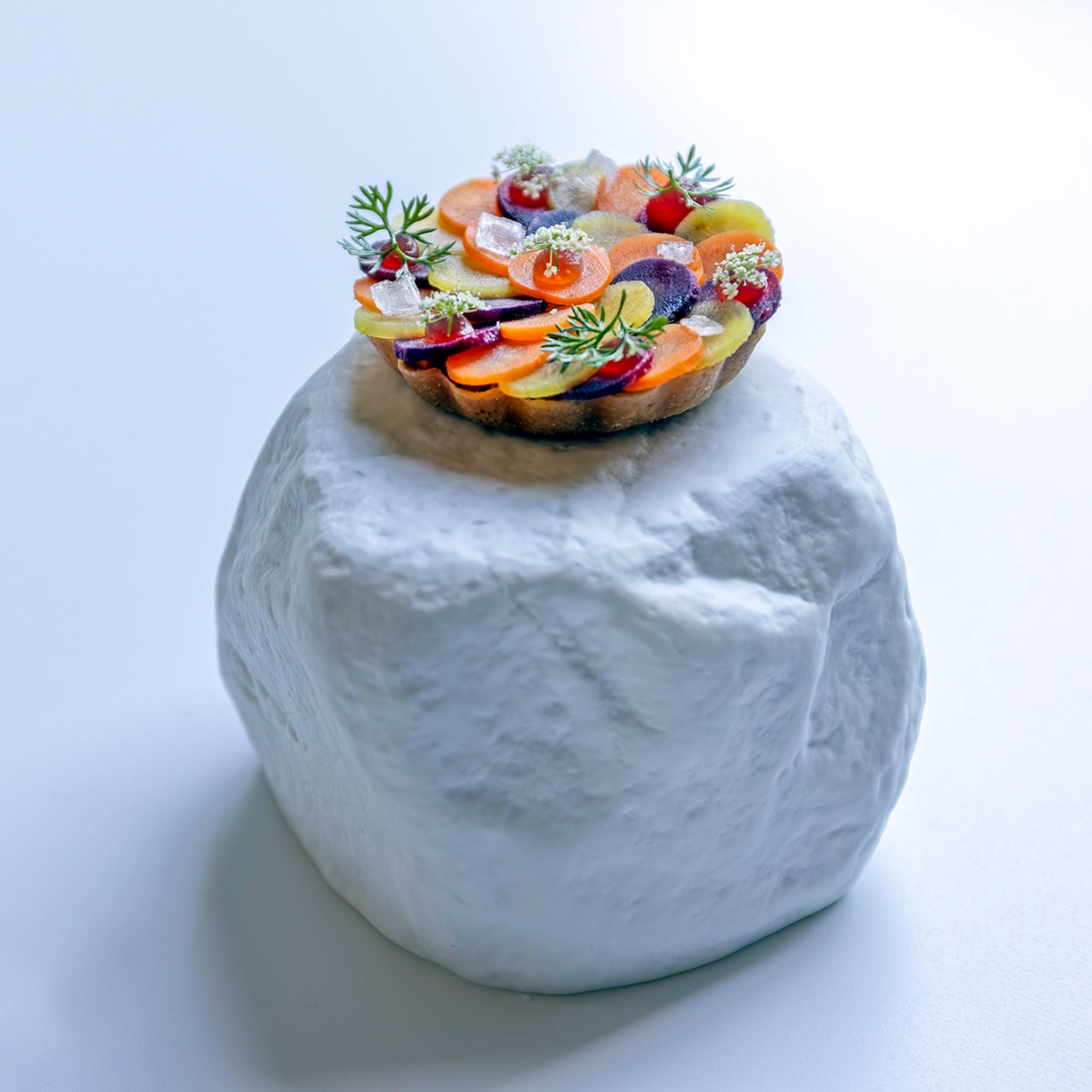 A tart of sliced vegetables and herbs set on a white block of stone