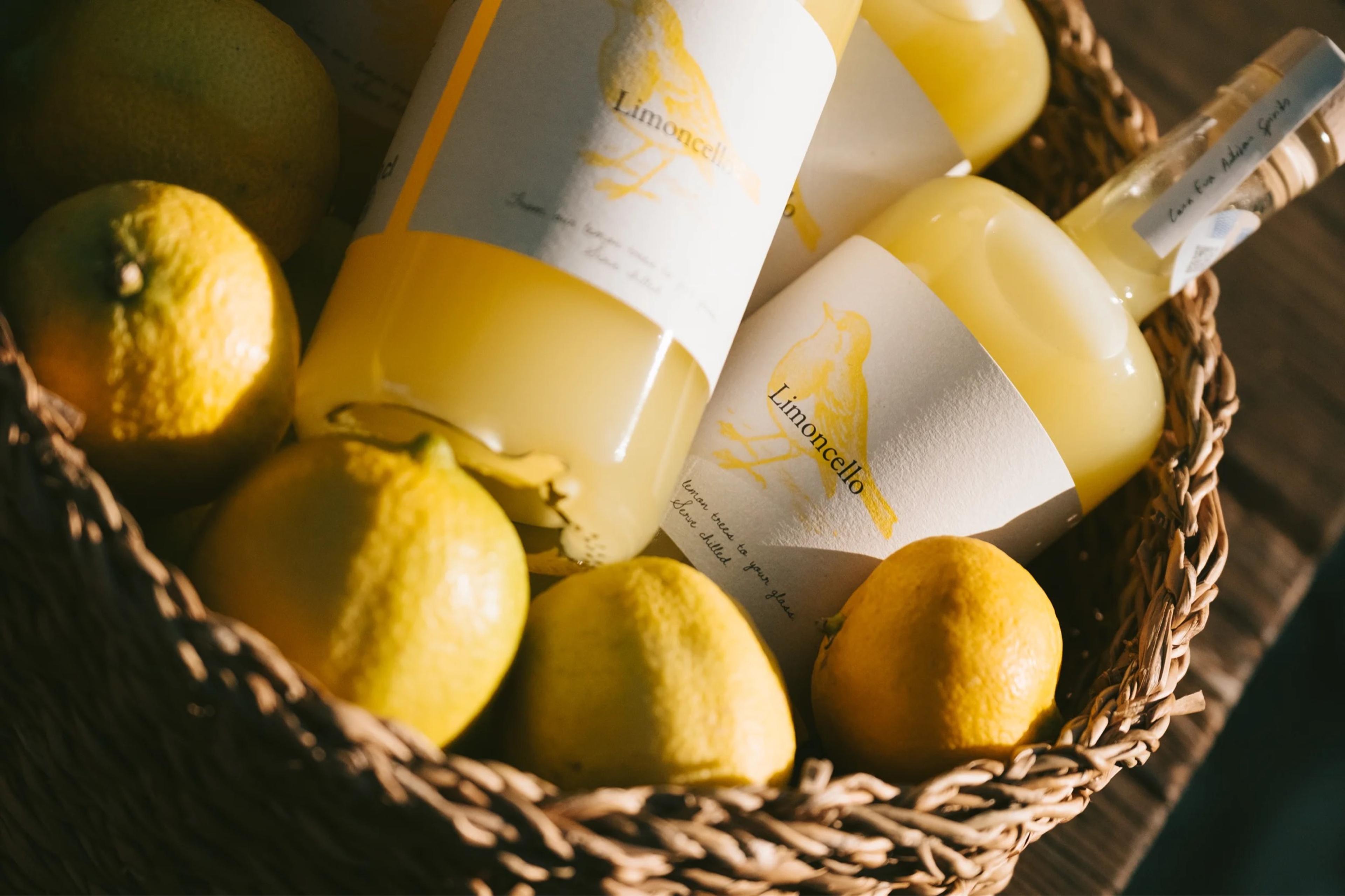 A basket of lemons and bottles of limoncello on a wooden table.