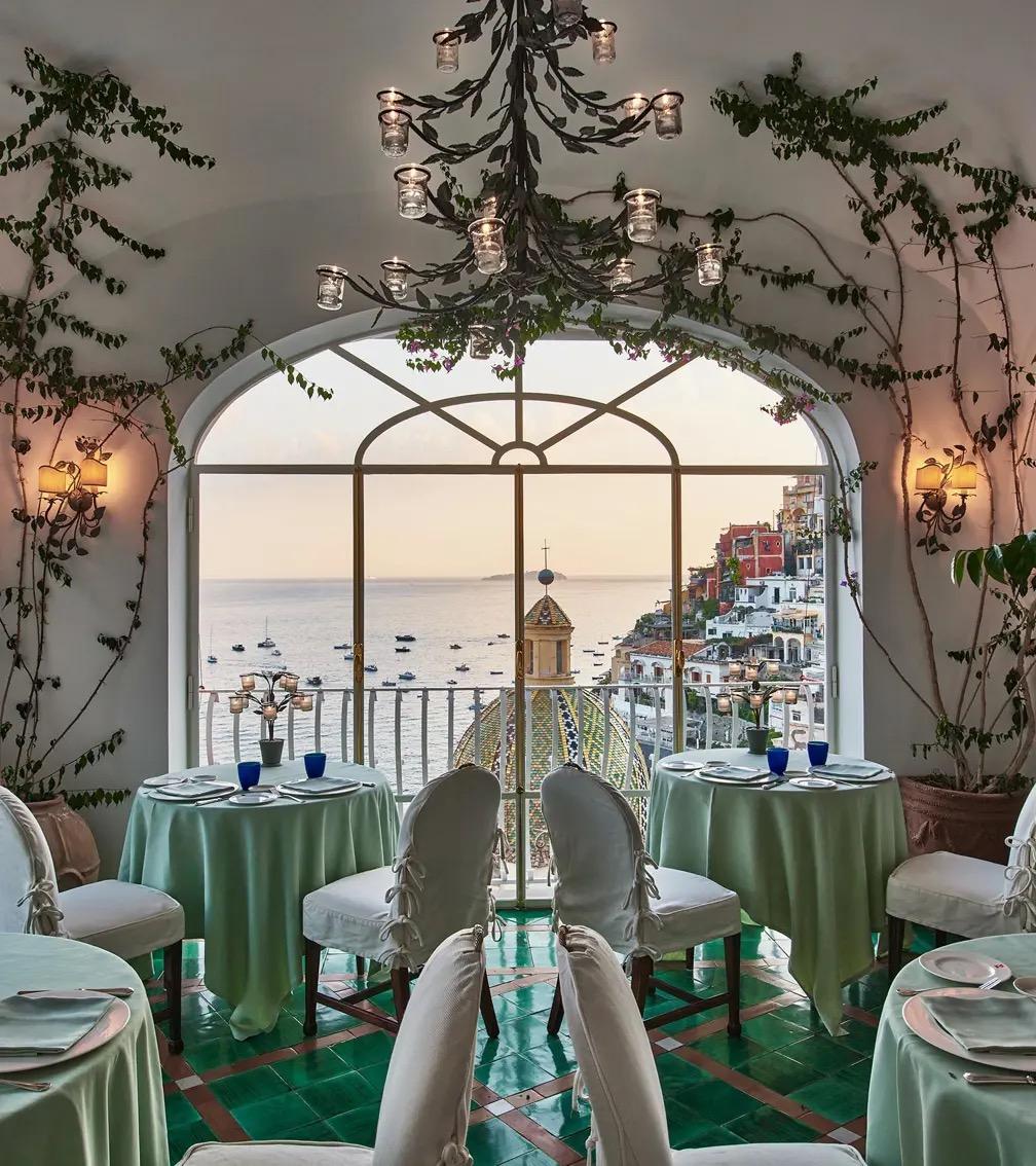 Tables laid in green under an arched window looking out over the sea and the town.