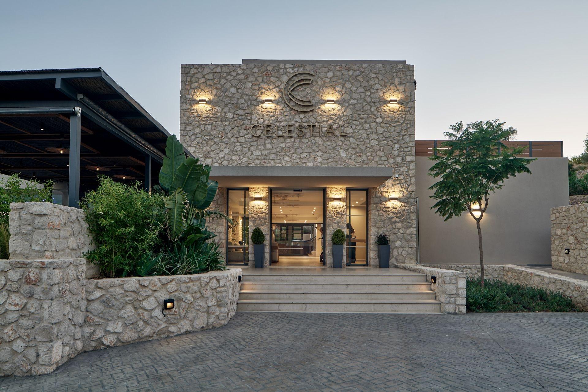 A stone-walled hotel entrance lit at dusk, with Celestial lettering above glass doors and steps leading up through planted borders.