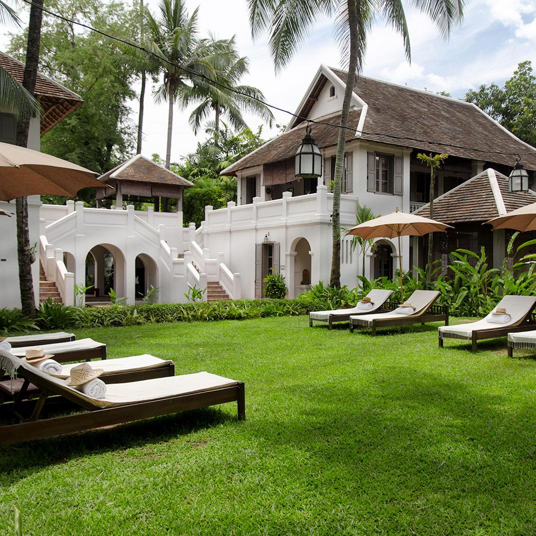 A white colonial house above a lawn with loungers
