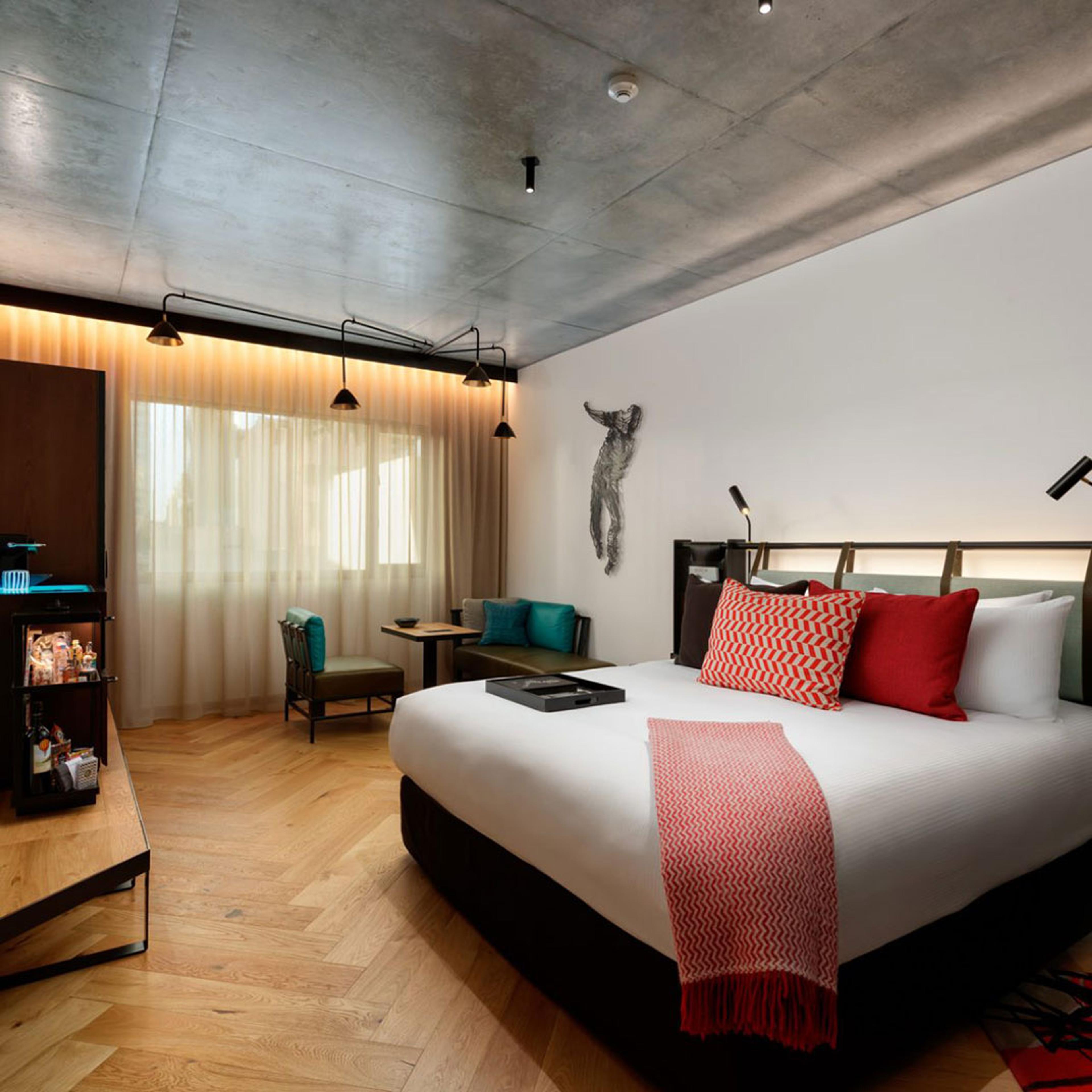 A bedroom with red cushions on a white bed and a sculpture on the wall