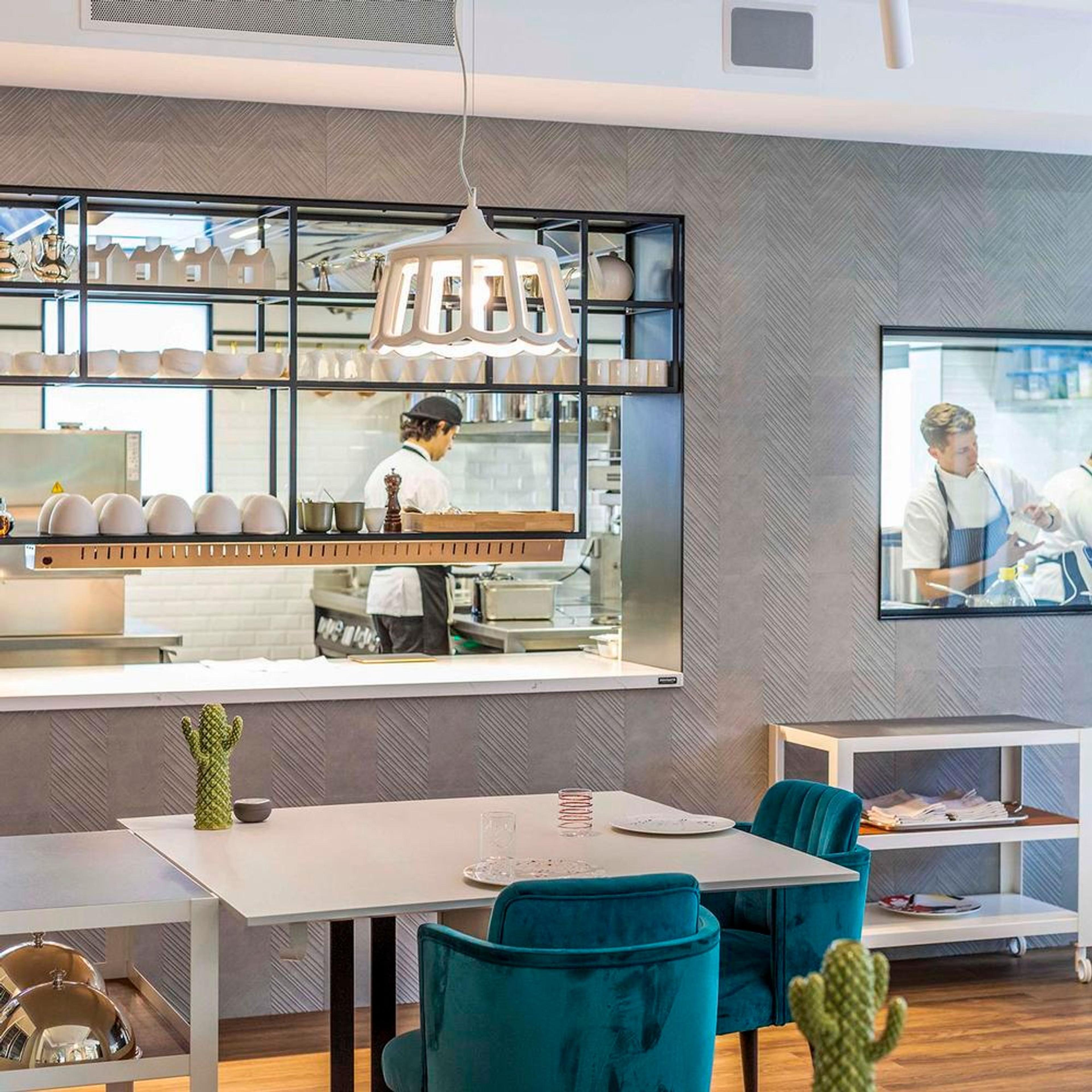 A pale dining room of round tables, a chef at work behind the glass of the open kitchen