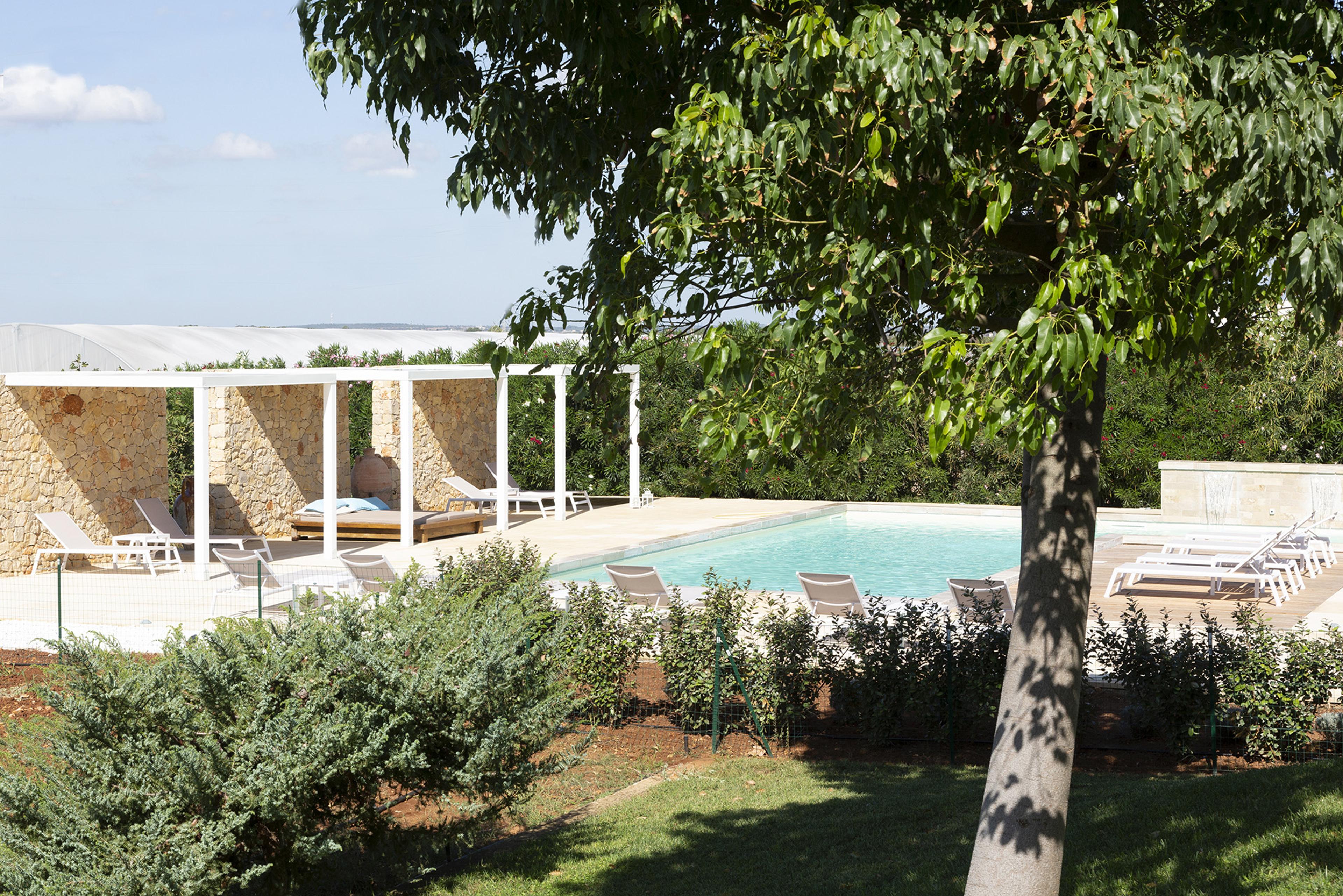 A pool and pergola seen past a tree, with lounge chairs and the flat Porto Cesareo landscape stretching to the horizon.