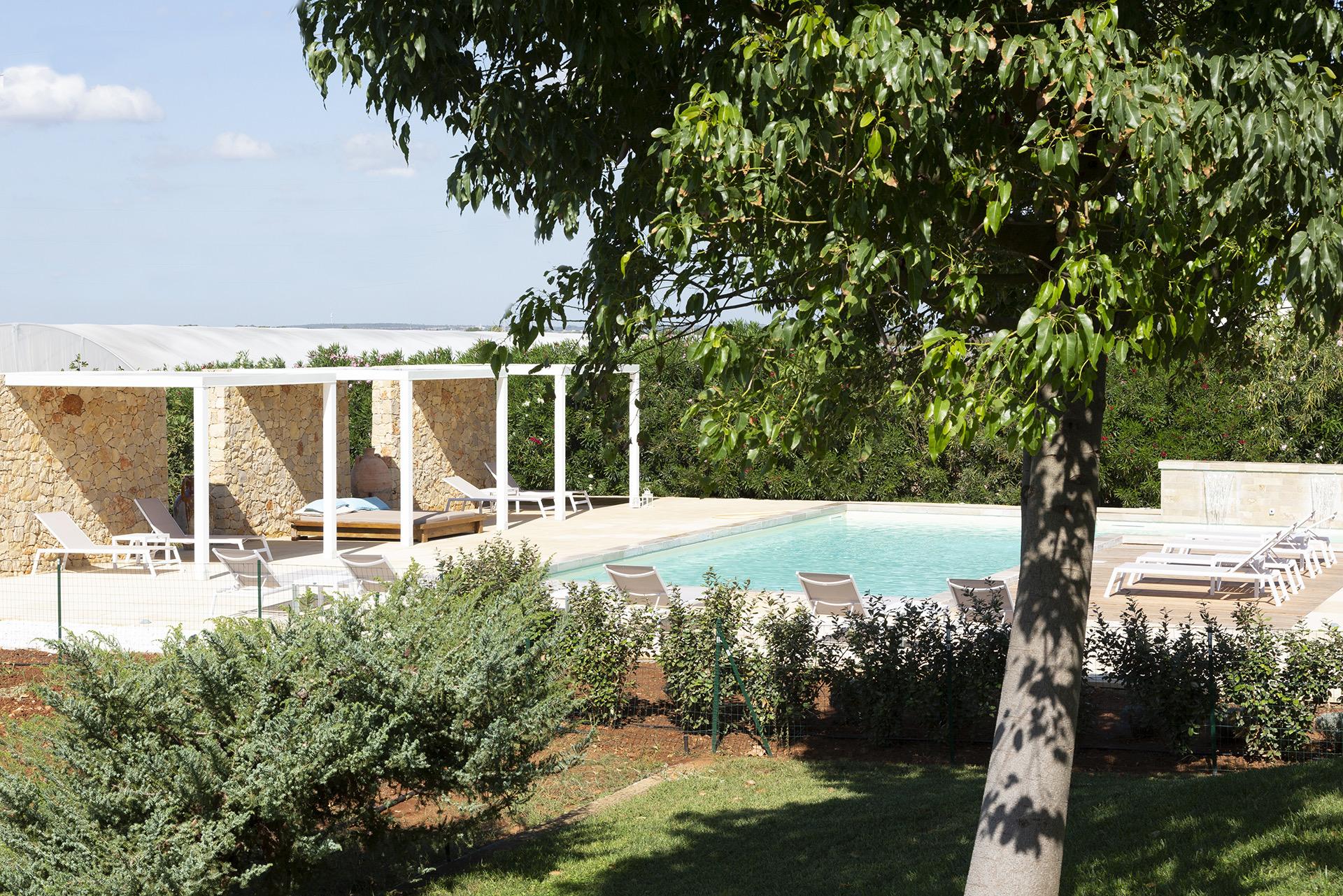 A pool and pergola seen past a tree, with lounge chairs and the flat Porto Cesareo landscape stretching to the horizon.