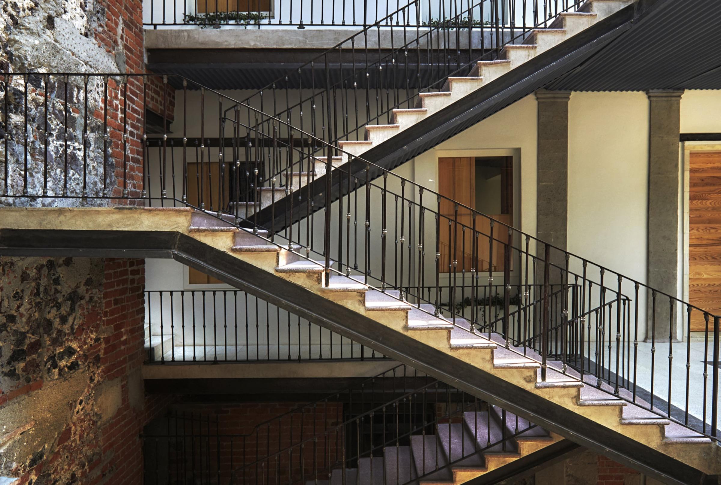 A multi-storey courtyard with black iron staircases zigzagging past brick and plastered walls and wooden doors.