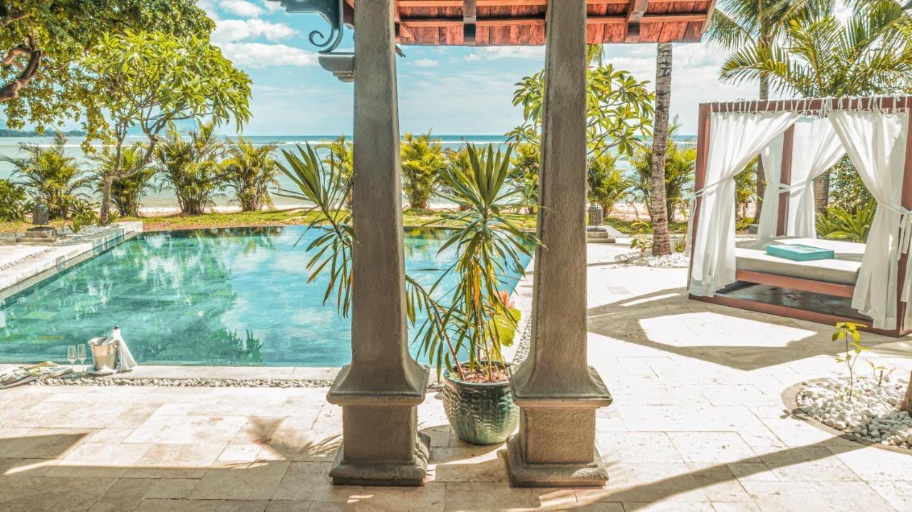 A pool between palm trunks with the sea beyond