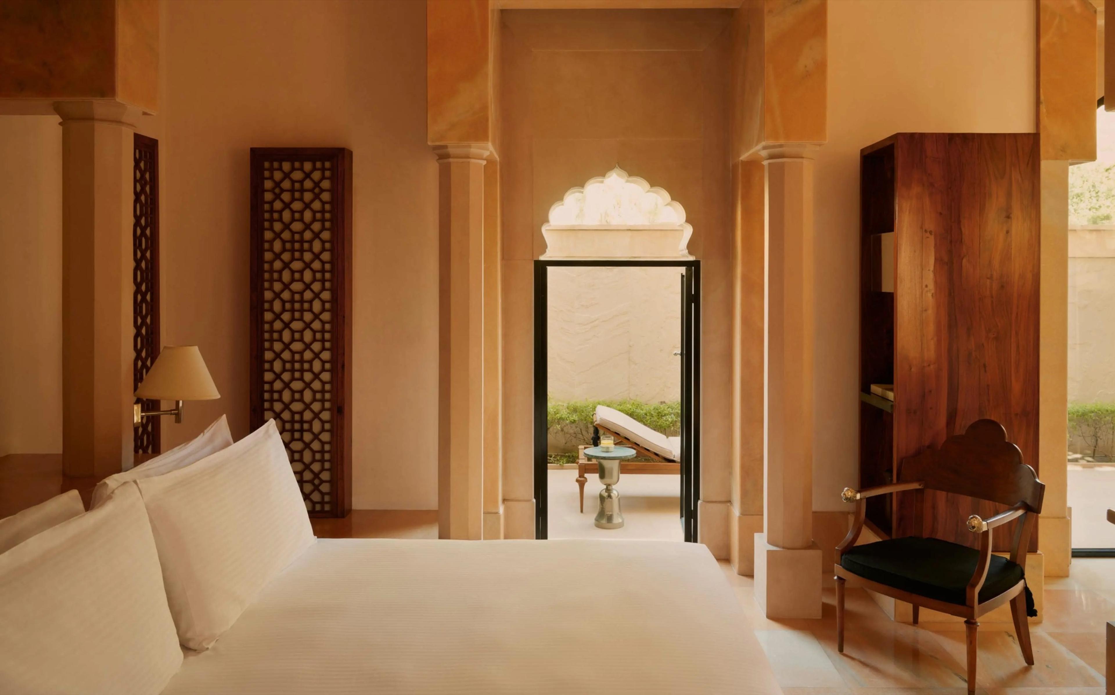 A bedroom with a wooden lattice screen and a carved archway opening onto a private terrace with a sun lounger.