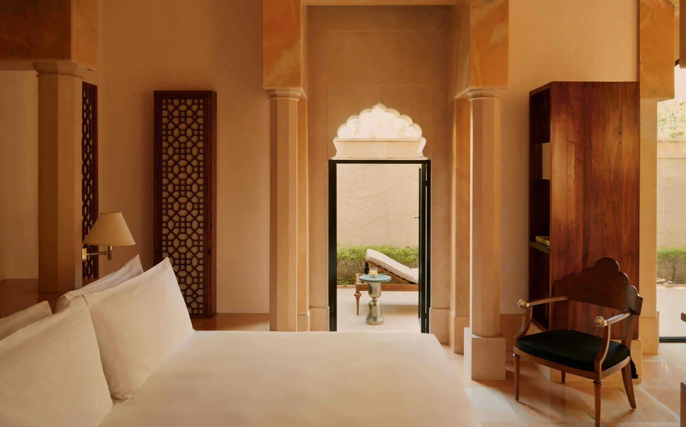 A bedroom with a wooden lattice screen and a carved archway opening onto a private terrace with a sun lounger.
