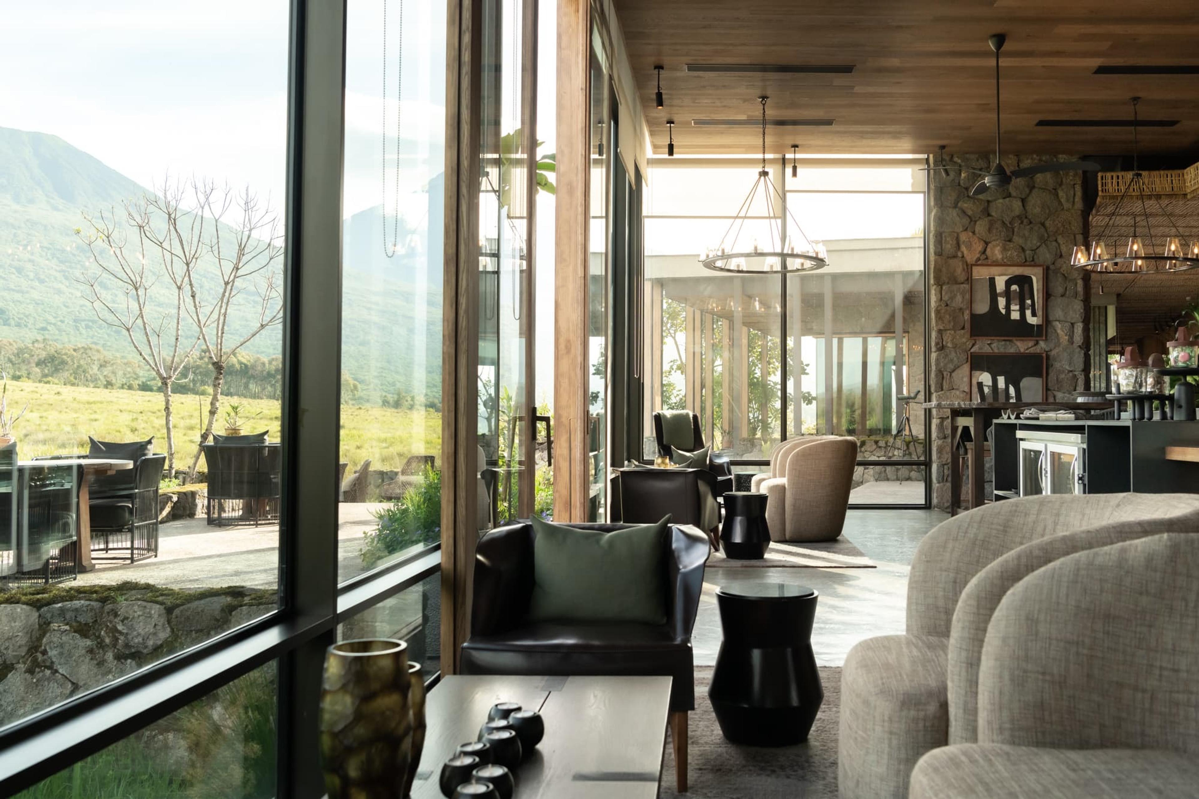 A lounge with a round pendant light and a stone pillar opens through floor-to-ceiling glass onto grassy hills.