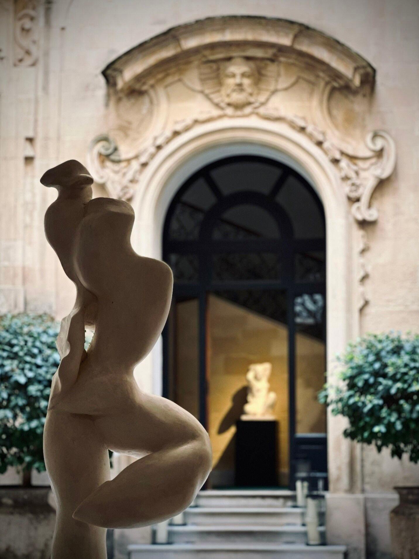 A stone female statue beside a Baroque doorway, with a second statue visible through the glass door behind it.
