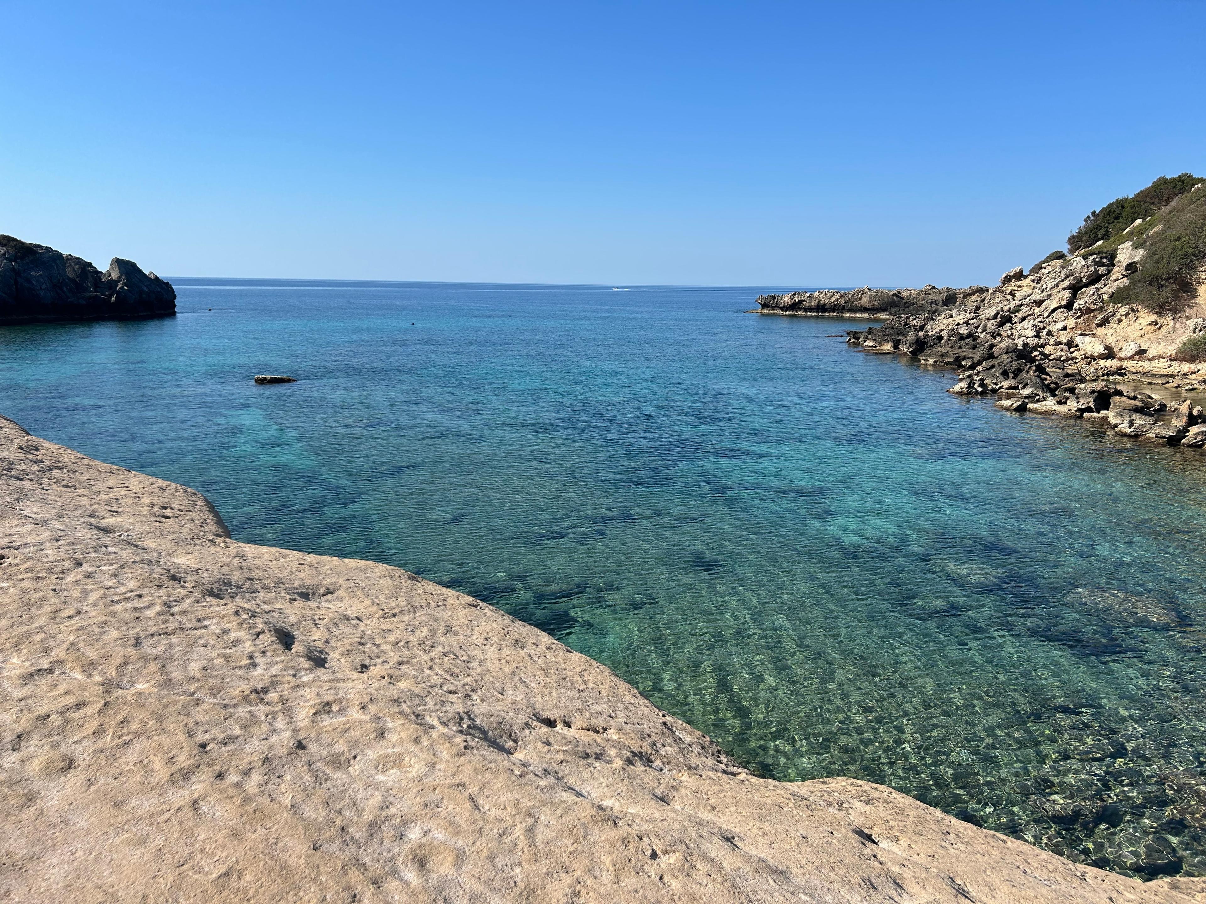 A rock-cut cove nearby with clear turquoise water over pale stone