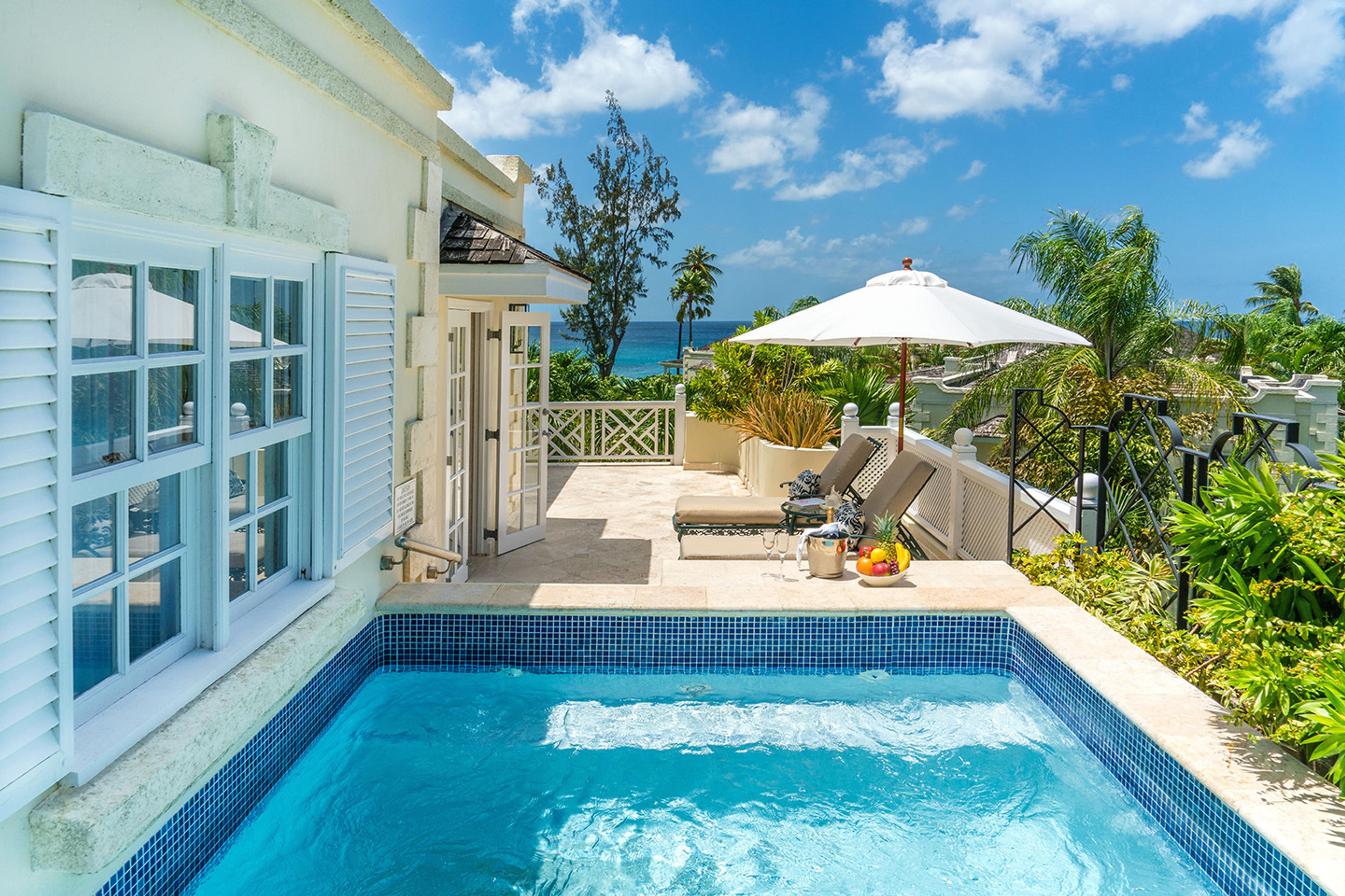 A private plunge pool on a terrace beside the hotel building, with sun loungers, a white umbrella and a bowl of fruit, and the sea visible beyond.