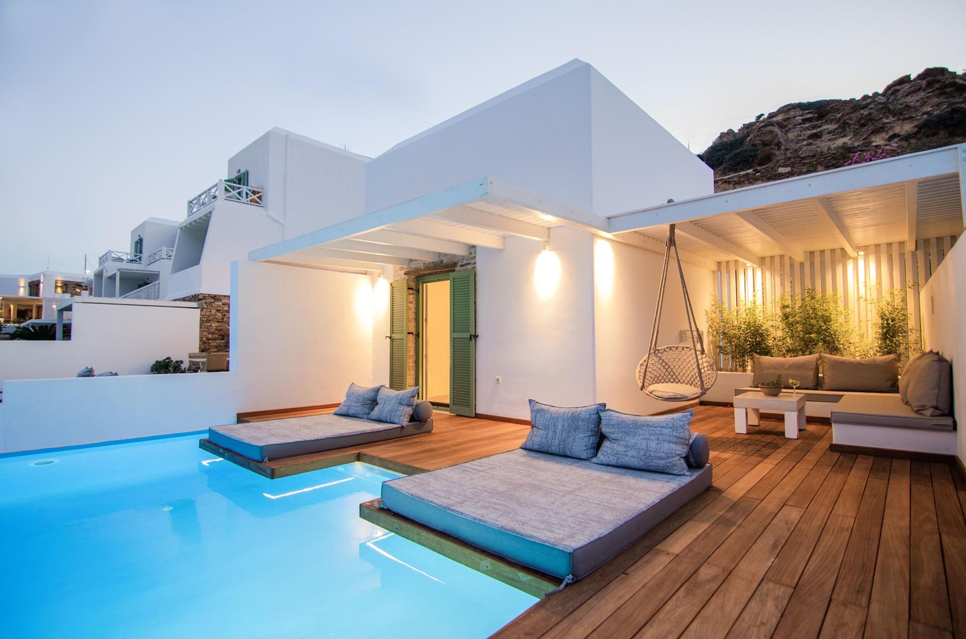 A private terrace at dusk with a small plunge pool, two raised cushioned daybeds on timber decking, and a hanging chair by the wall.